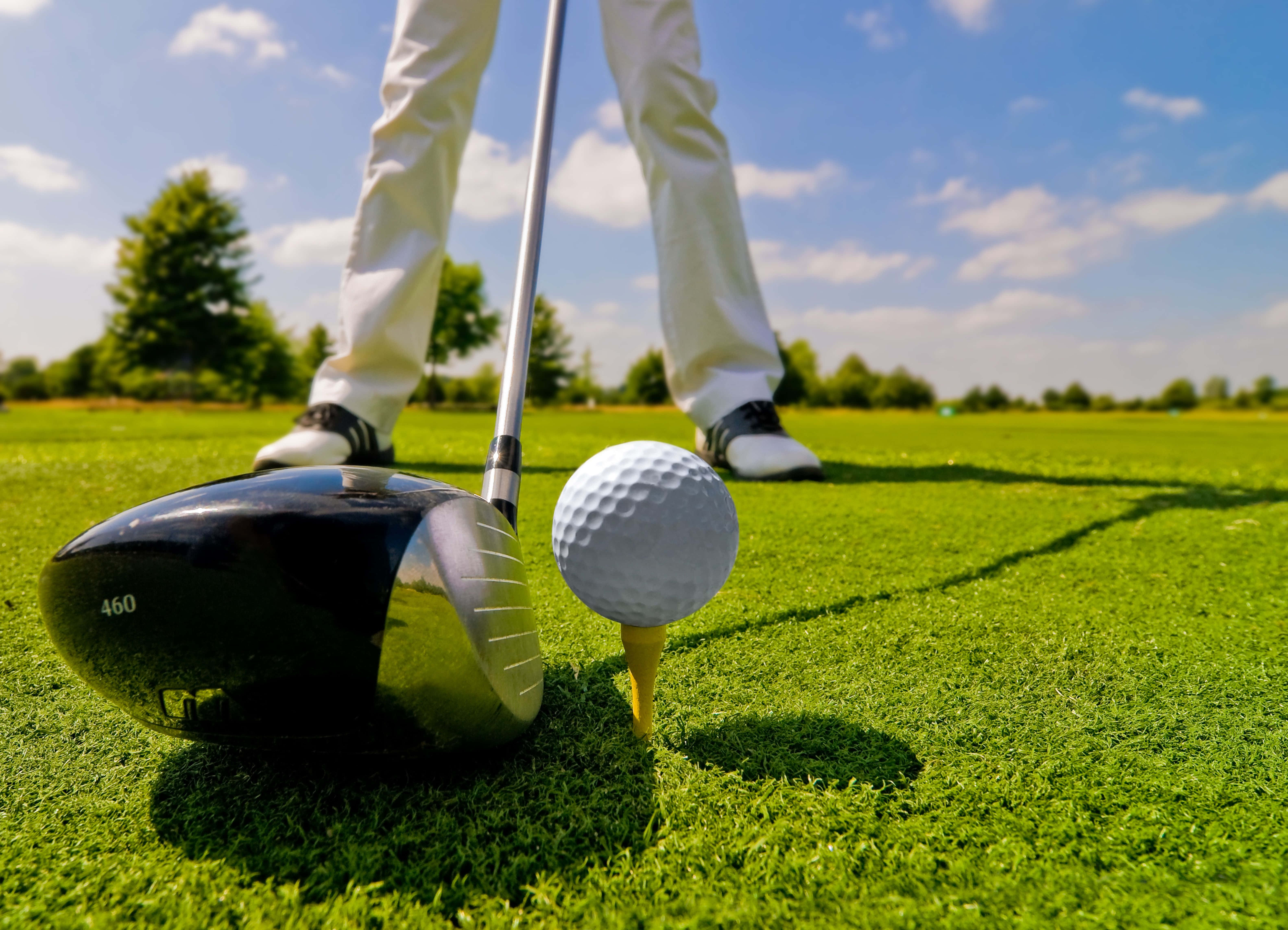 Golf 3840x1080 桌布 壁紙 — 一名高爾夫球手在充滿活力的綠色球道上，在藍天白雲下，準備好揮動一號木桿。