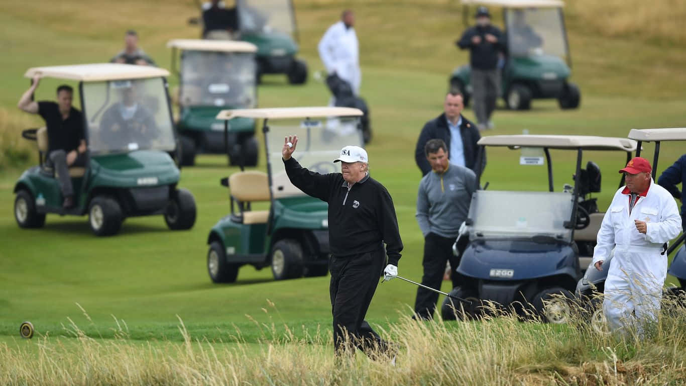 1366x768 Golf Course 桌布 壁紙 — 一名高爾夫球手在穿過翠綠的球場時向觀眾揮手，背景有高爾夫球車。