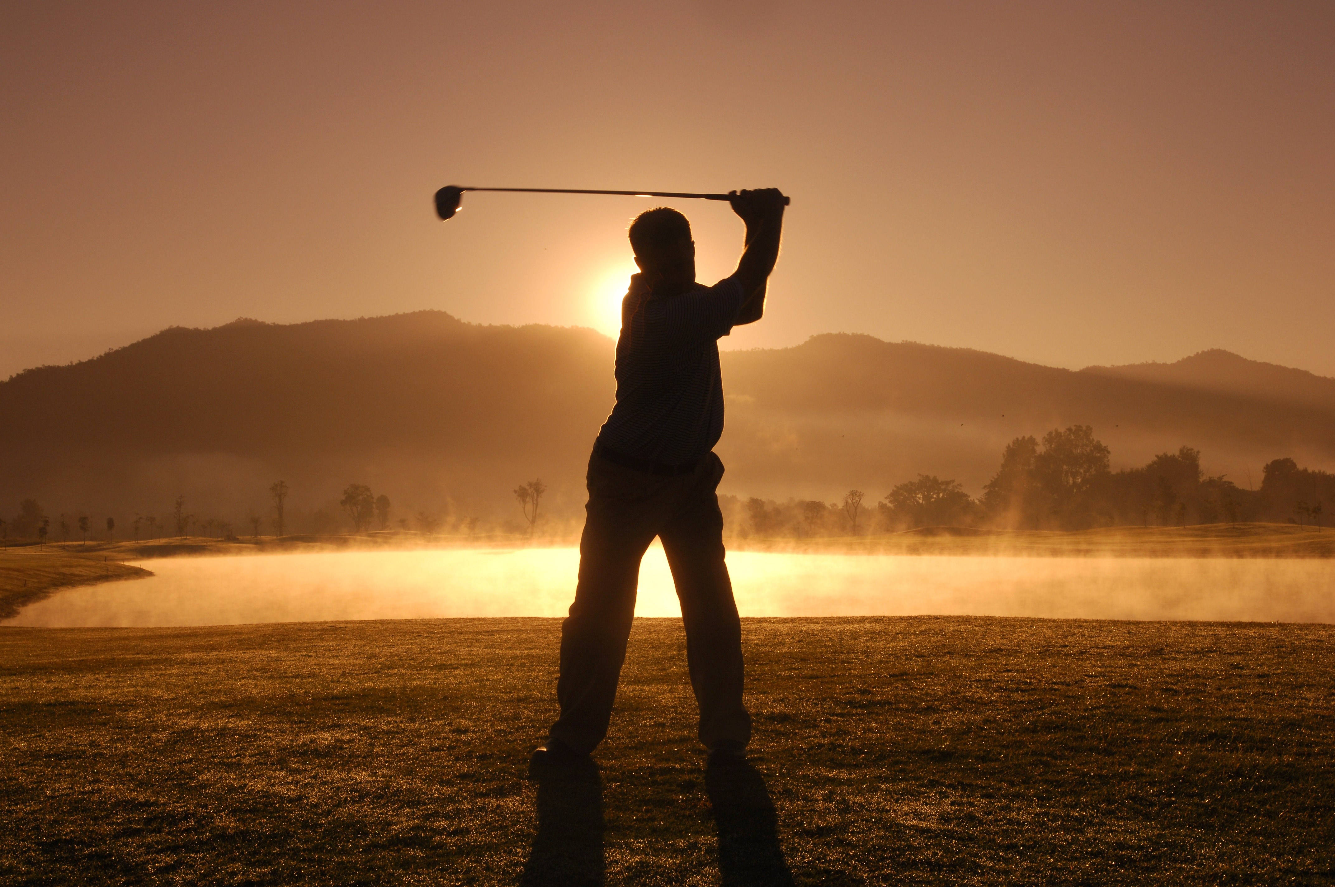 Golfing 桌布 壁紙 — 一名高爾夫球手在霧氣瀰漫的球場上，背對金色日出和遠山形成剪影。