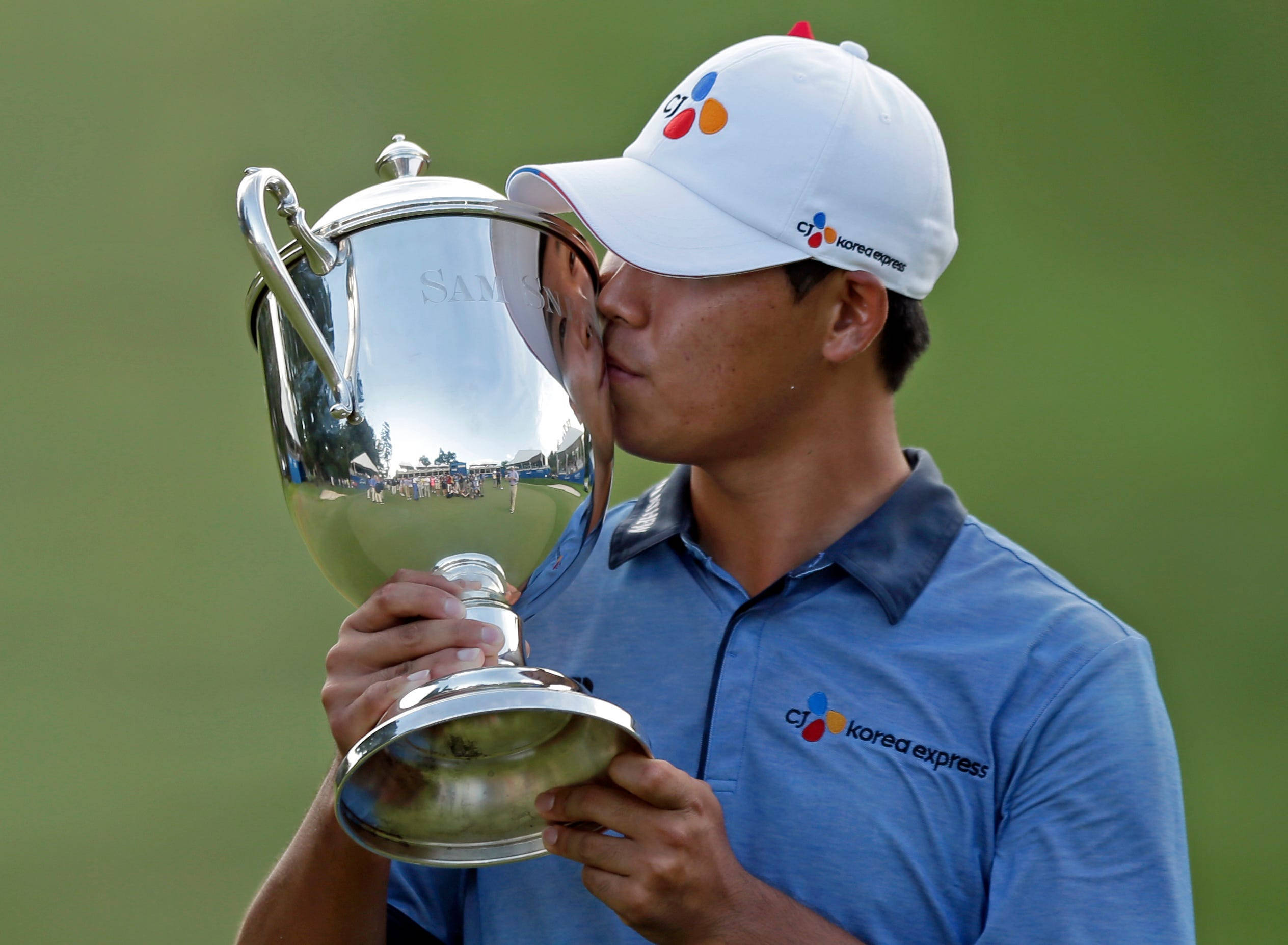 Trophy 桌布 壁紙 — 一名高爾夫球手戴著白色帽子和藍色Polo衫，在模糊的綠色背景下親吻閃亮的銀色獎盃。