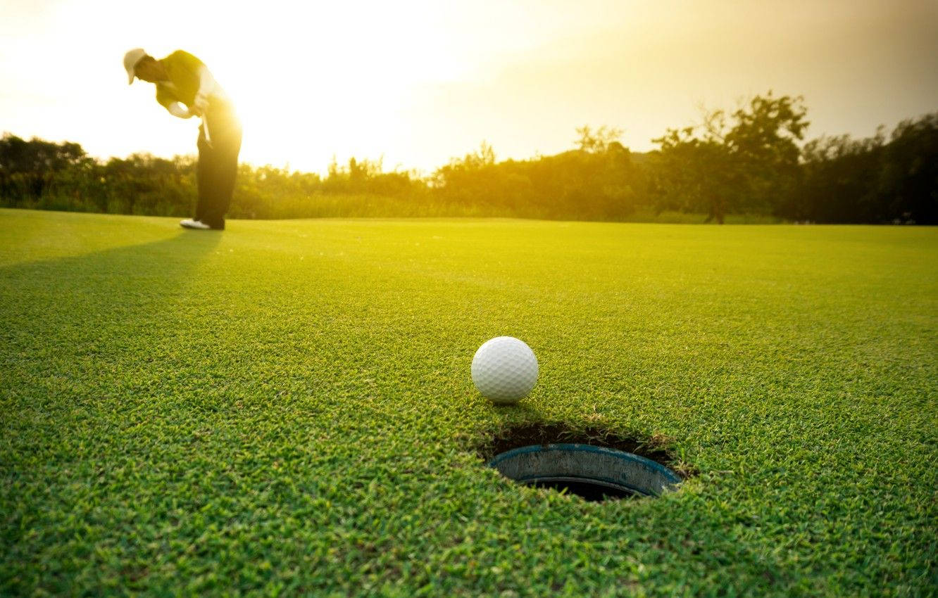 Golfing 桌布 壁紙 — 一名高爾夫球手的剪影，在夕陽西下時，於翠綠的球道上準備推桿入洞。