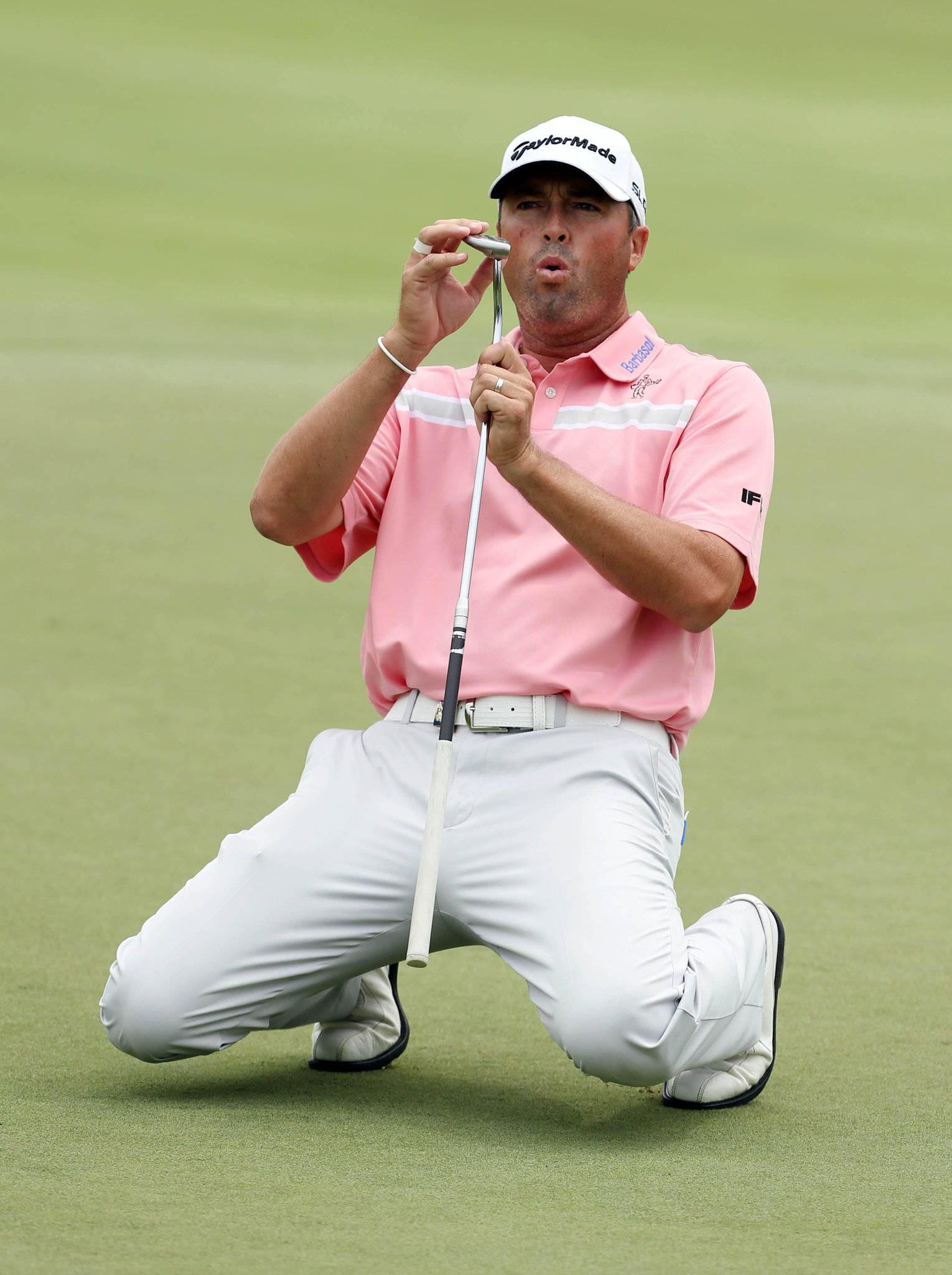 Ryan Palmer 桌布 壁紙 — 一名高爾夫球手跪在綠色高爾夫球場上，握著推桿並向桿頭吹氣。