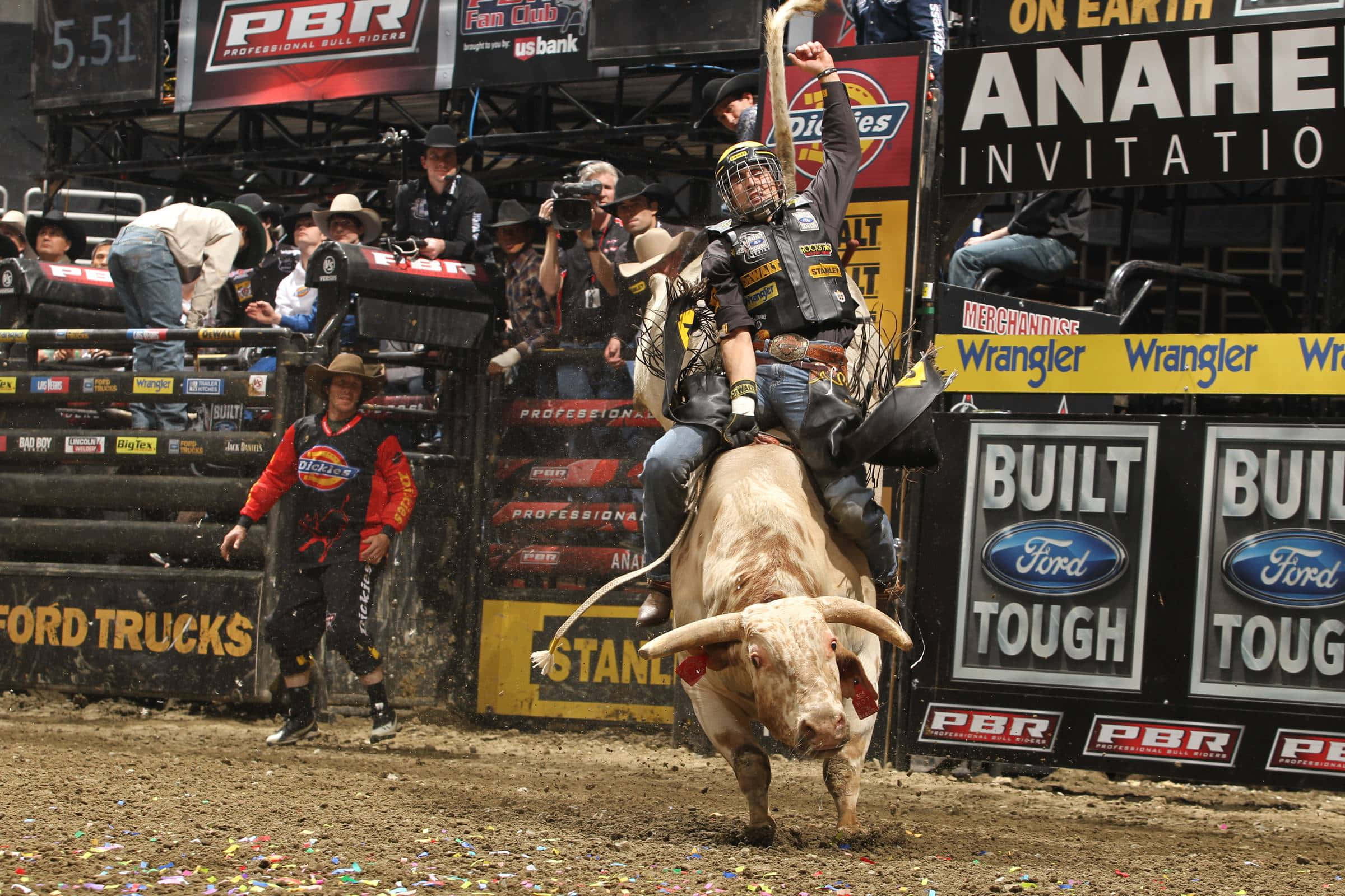 Bull Rider 桌布 壁紙 — 一名鬥牛騎士緊抓著一頭猛烈的公牛，在充滿觀眾和贊助商橫幅的牛仔競技場中，五彩紙屑如雨般落下。