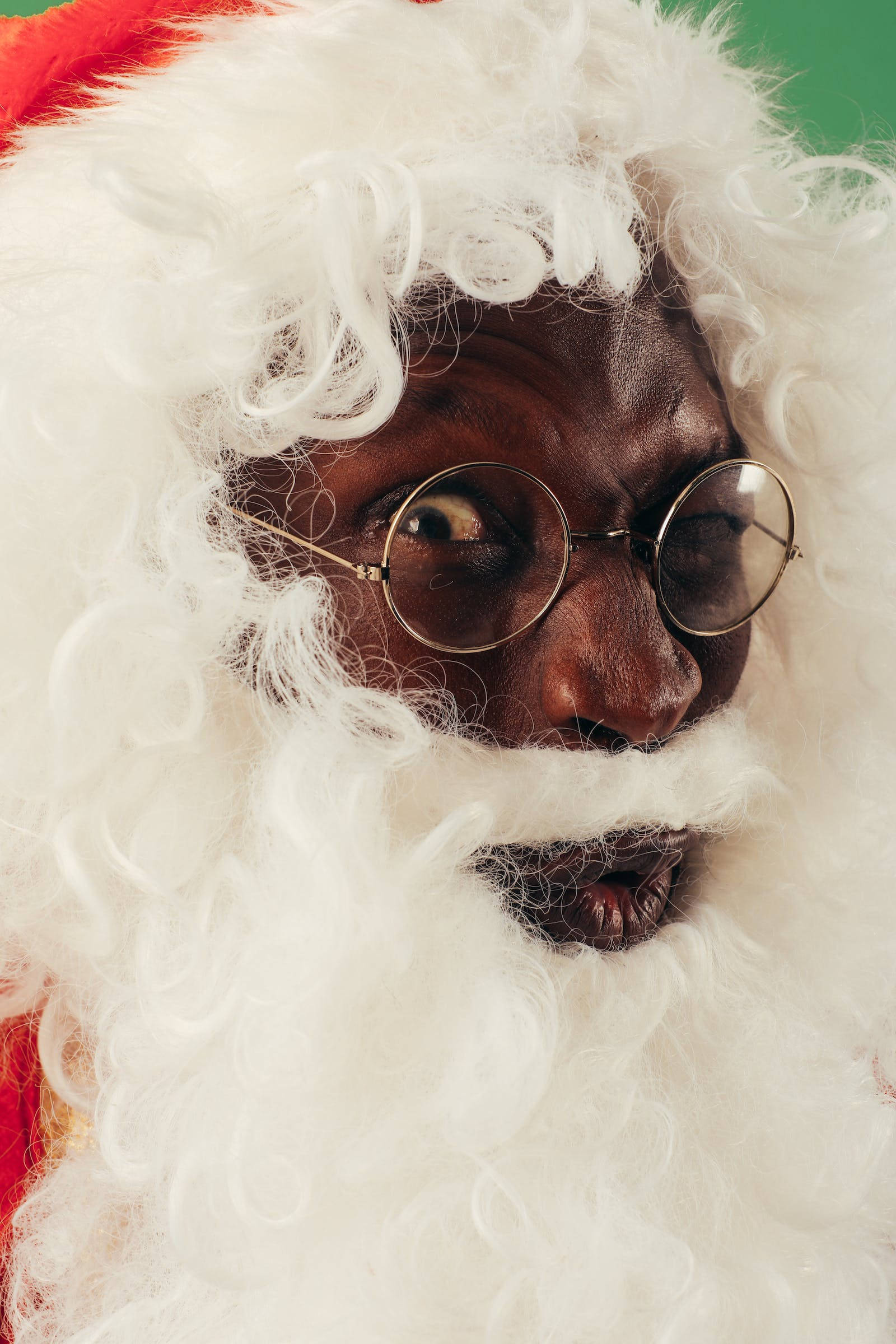 Santa Claus 桌布 壁紙 — 一名黑人男子打扮成聖誕老人，戴著圓框眼鏡和 fluffy 白色鬍鬚，在綠色背景前的特寫。