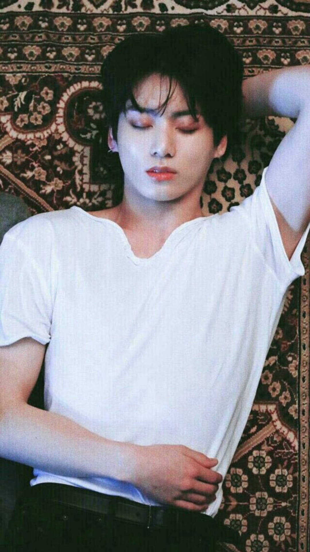 桌布 壁紙 — 一名黑髮年輕男子身穿白色T恤，頭向後靠在華麗圖案地毯上。