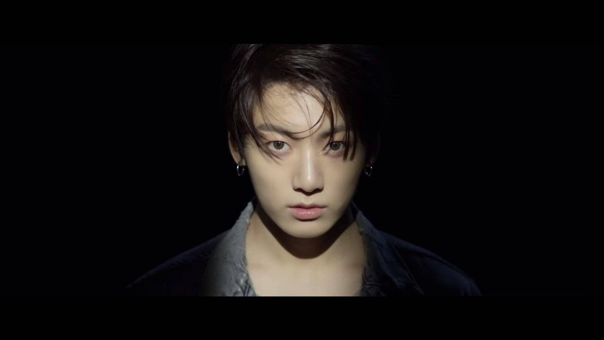 Jungkook 桌布 壁紙 — 一名黑髮戴耳環的年輕男子在戲劇性聚光燈下，對著黑色背景凝視。