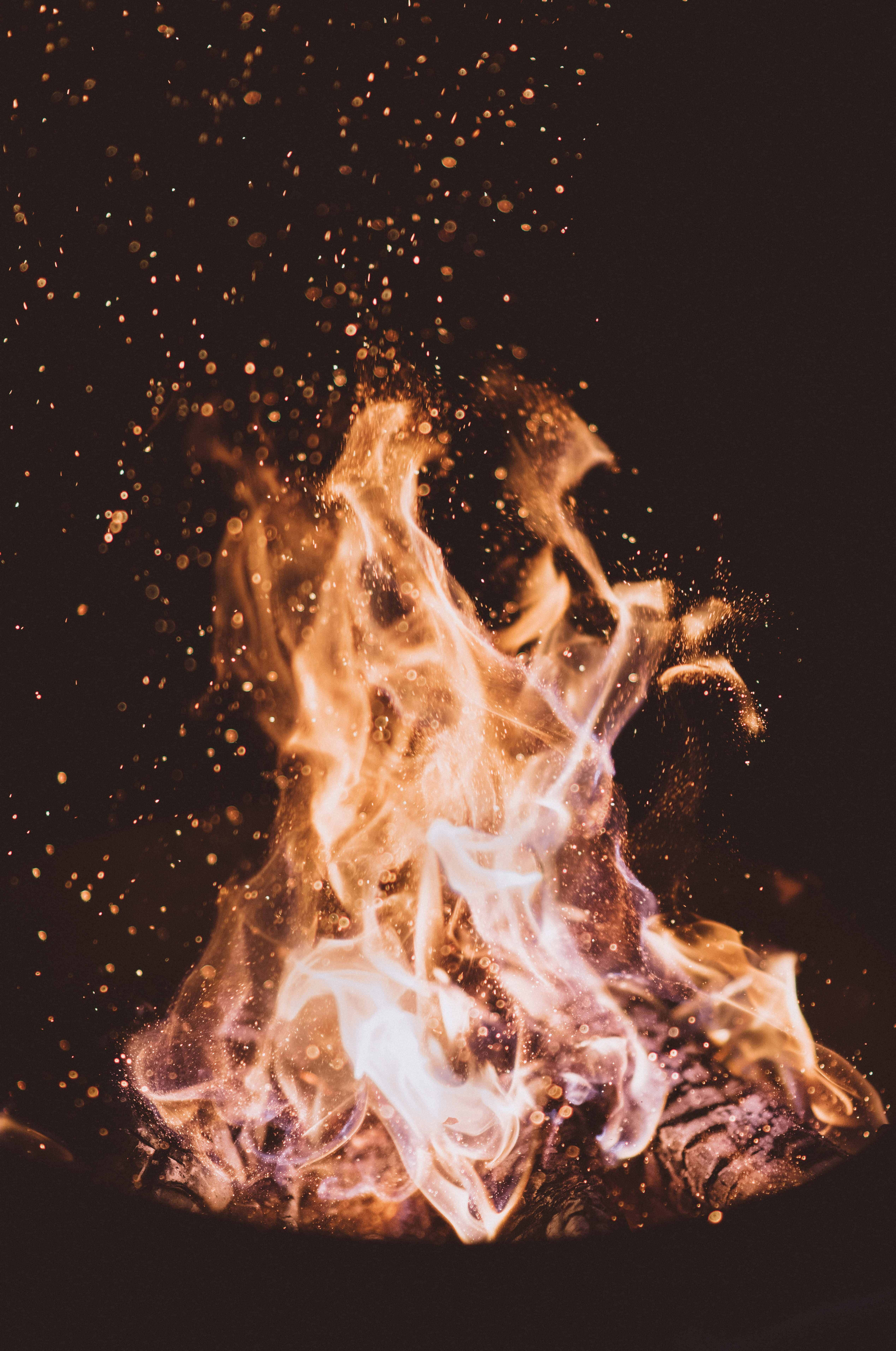 火焰動畫 桌布 壁紙 — 一團充滿活力的火焰在黑暗背景中燃燒，橙色和白色的火焰舞動，將發光的餘燼送入空中。
