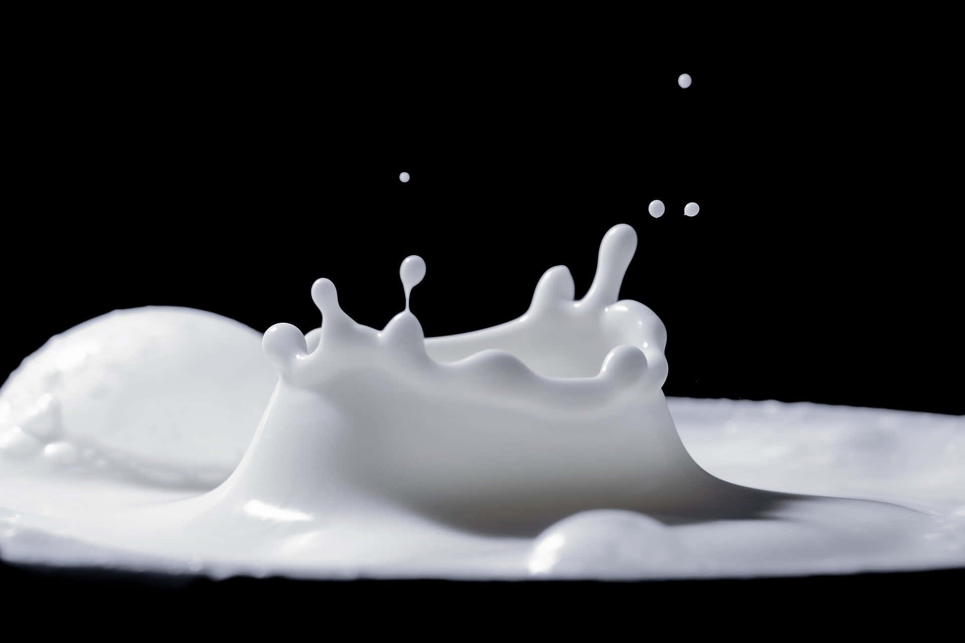 Milk 桌布 壁紙 — 一團冰凍般的乳白色液體在純黑背景上噴濺開來，水滴懸浮在半空中。