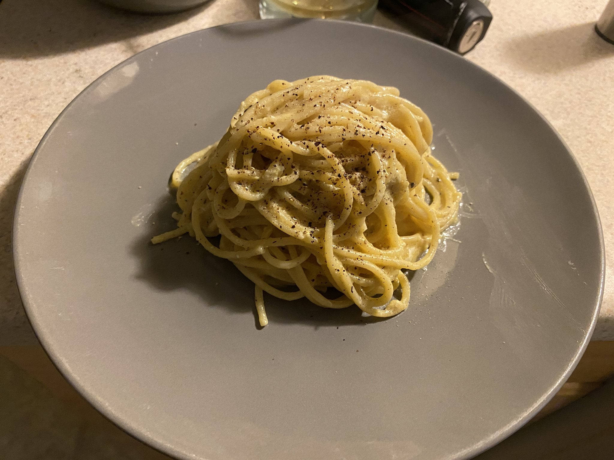 烹飪 桌布 壁紙 — 一團奶油義大利麵配黑胡椒，在溫暖的室內燈光下置於灰色盤子中央。