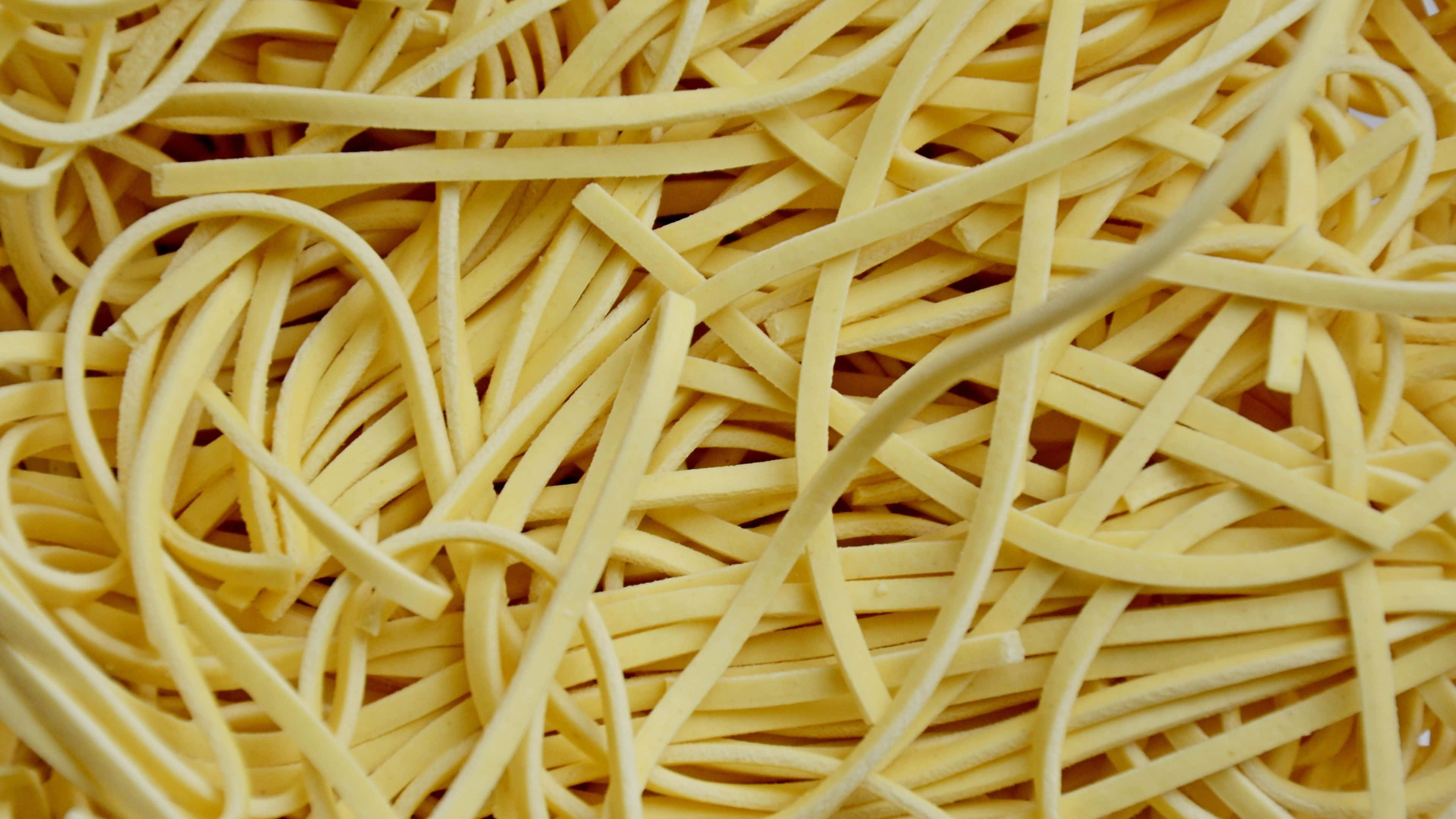 Noodles 桌布 壁紙 — 一團淡黃色義大利麵條纏繞在一起的特寫，營造出有紋理的食物背景。