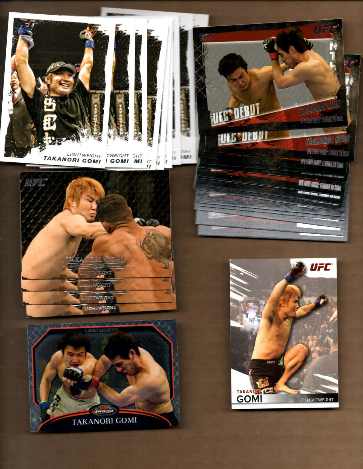 UFC 桌布 壁紙 — 一堆UFC收藏卡，展示拳手高森剛志在棕色表面上以各種戰鬥姿勢出現。