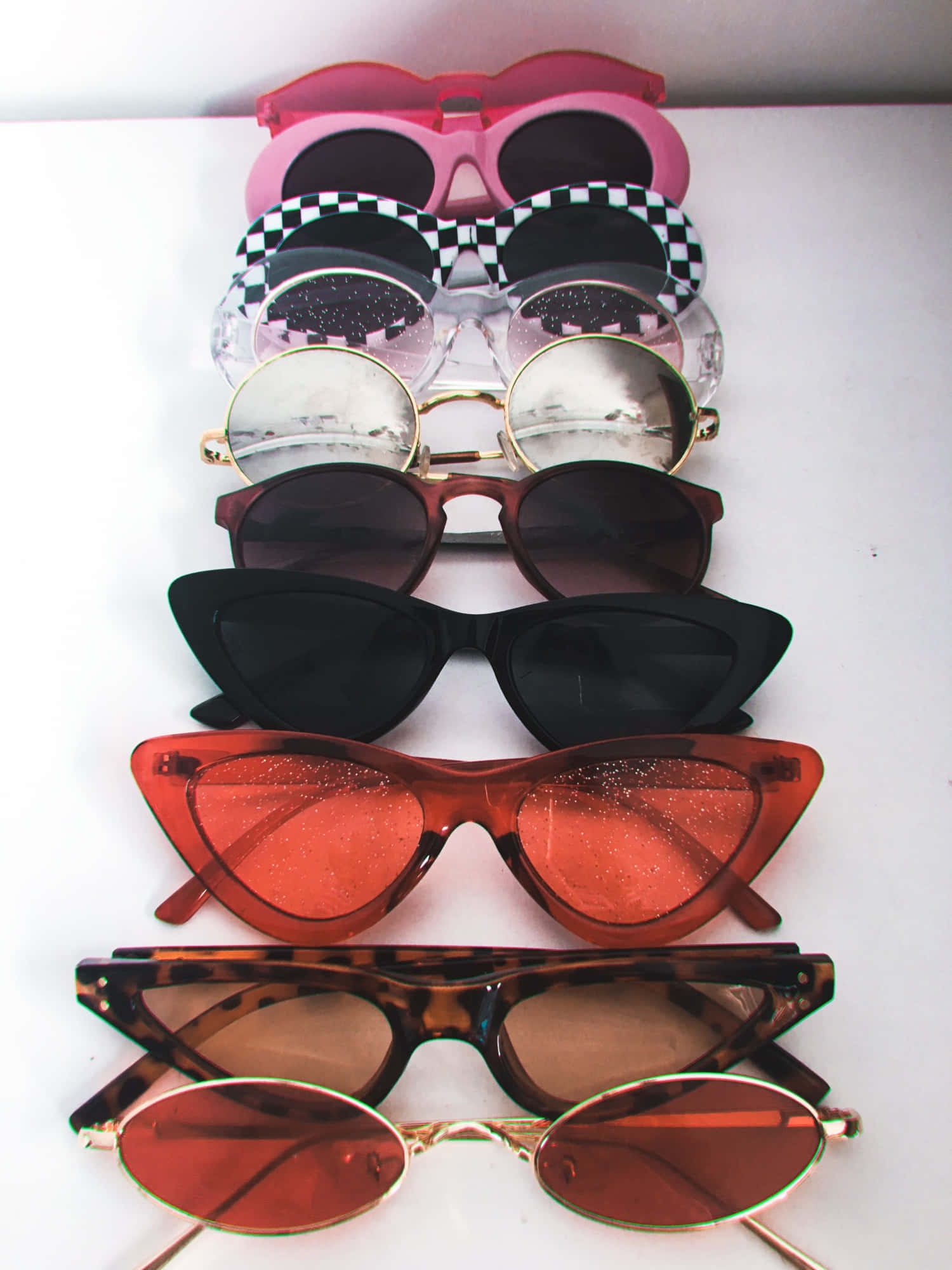 Sunglasses 桌布 壁紙 — 一堆七款時尚太陽眼鏡，形狀和顏色各異，整齊排列在白色表面上。