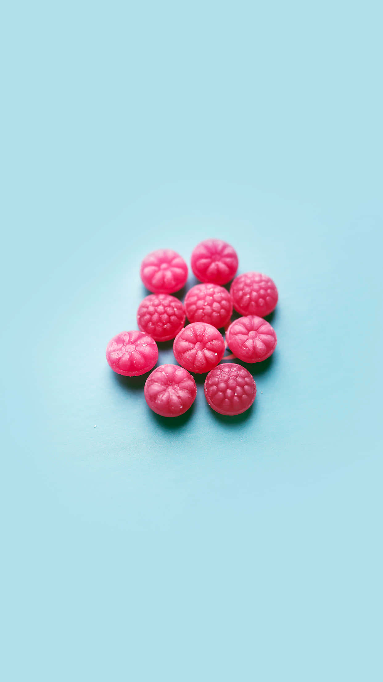 Cute Food iPhone 桌布 壁紙 — 一堆亮粉紅色覆盆子形狀的糖果放在柔和的粉藍色表面上。