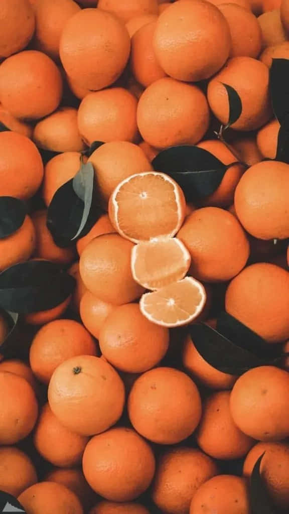 Cool Orange 桌布 壁紙 — 一堆充滿活力的完整和半個柳橙，深色葉子散落各處。