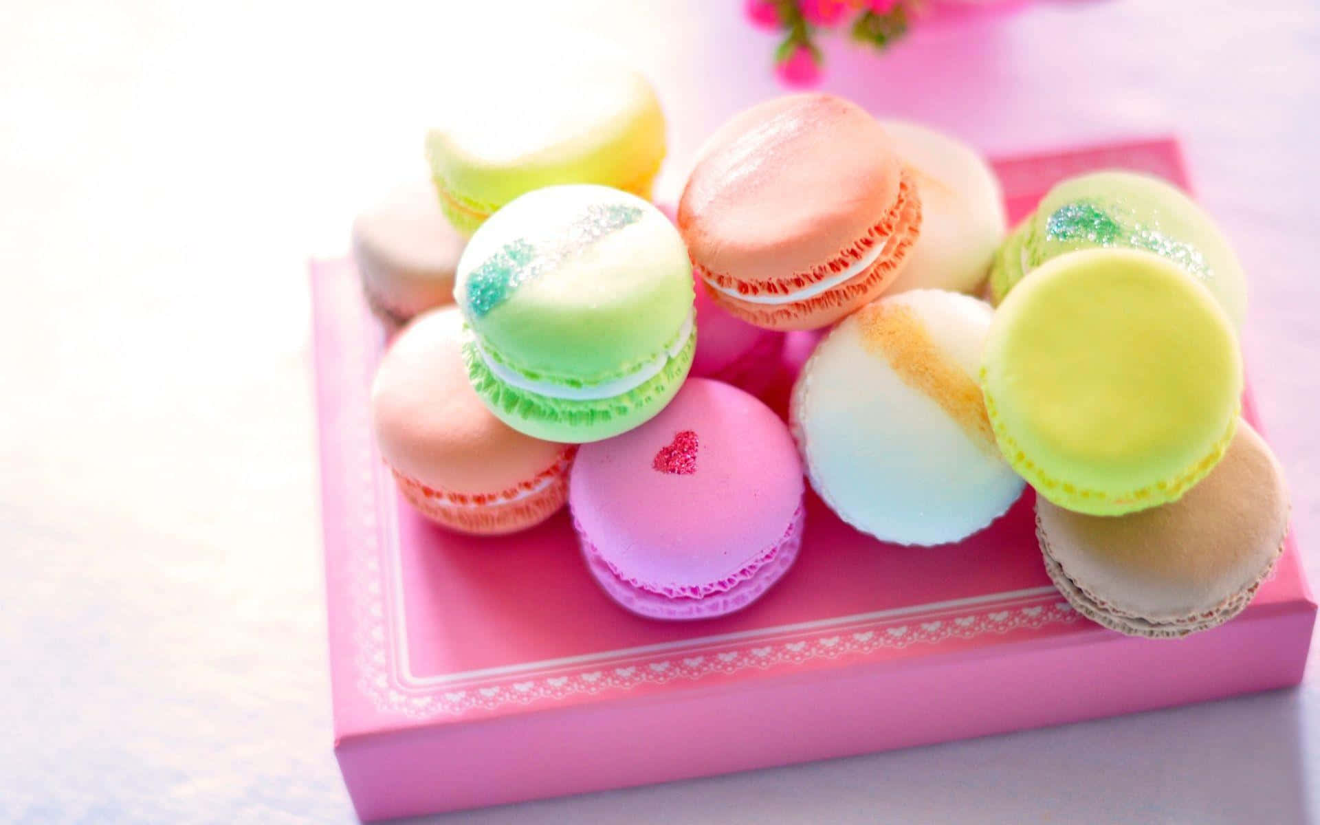 Pastry 桌布 壁紙 — 一堆充滿活力的粉紅、綠色和黃色馬卡龍放在一個裝飾性的粉紅盒子上，背景是柔和的花卉圖案。