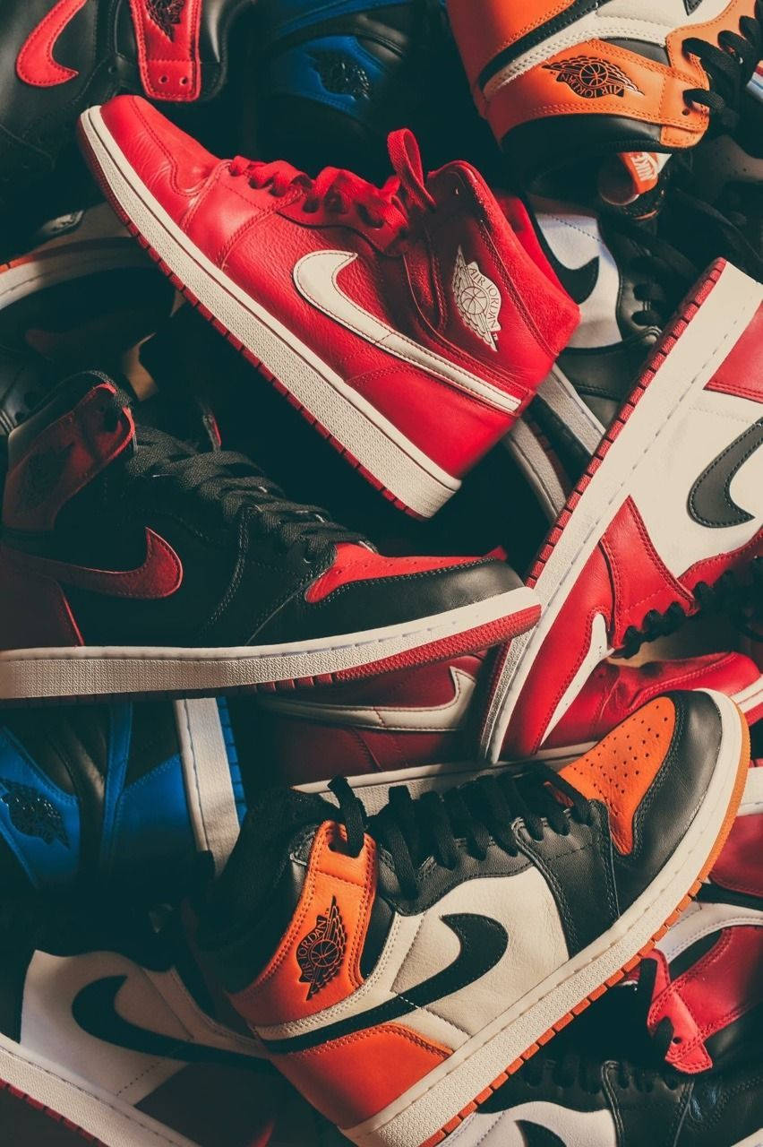 Air Jordan 桌布 壁紙 — 一堆充滿活力的紅色、黑色和橙色 Air Jordan 運動鞋，展示標誌性的 swoosh 和 wing 標誌。