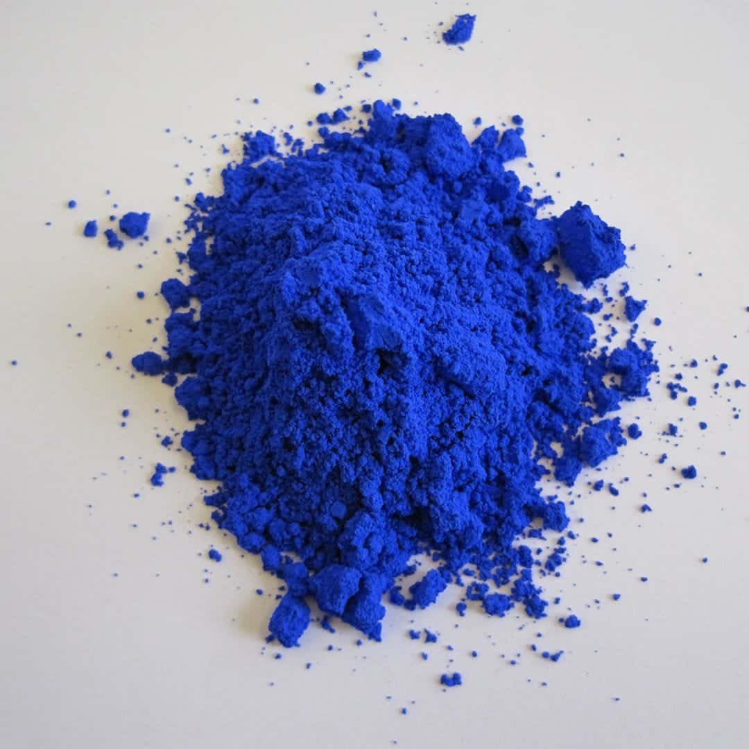 Indigo Blue 桌布 壁紙 — 一堆充滿活力的電光藍色粉末散落在純白色表面上，細小顆粒向外輻射。