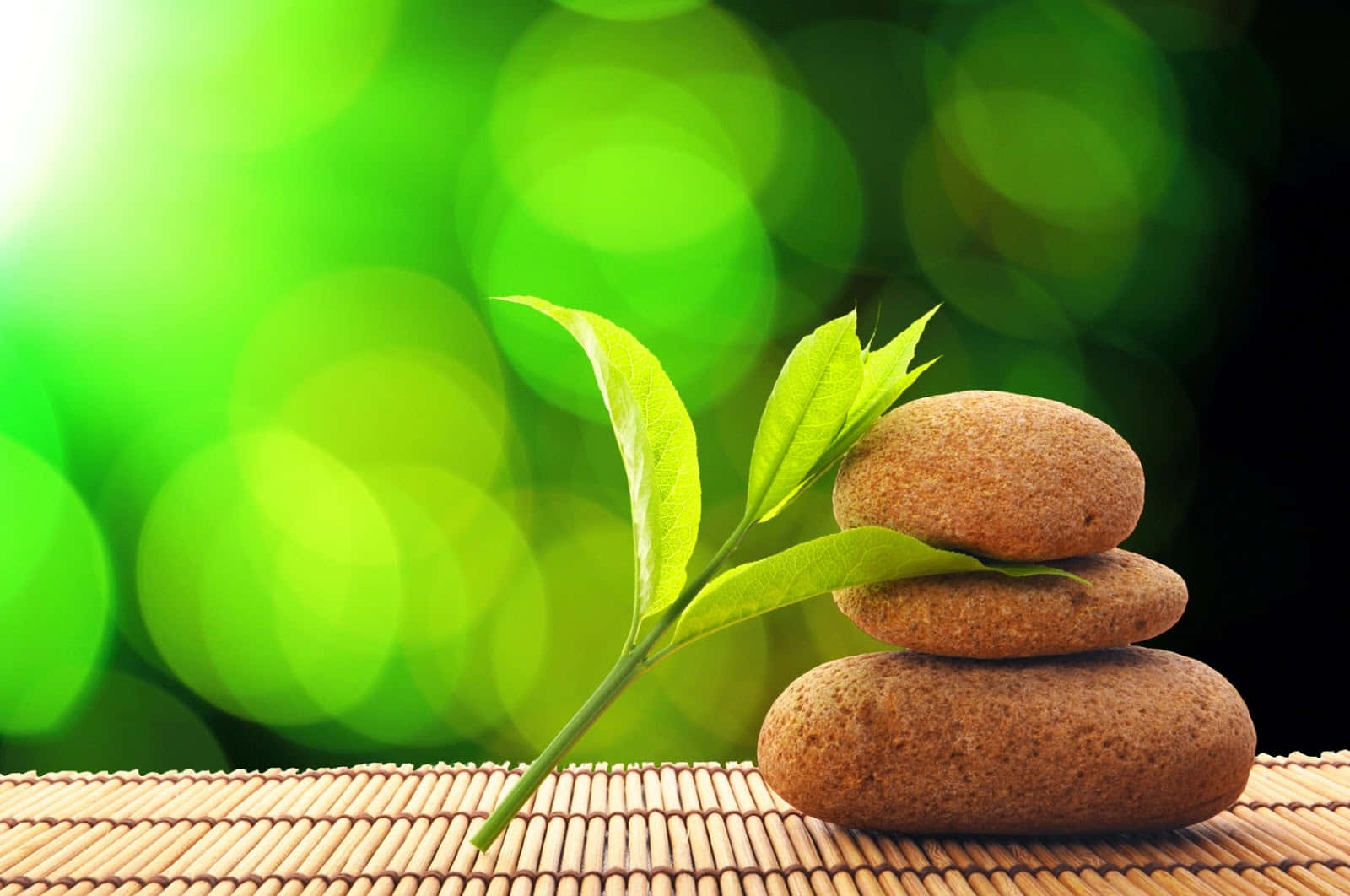 禪 桌布 壁紙 — 一堆光滑的棕色石頭和新鮮的綠葉放在竹蓆上，背景是發光的綠色散景。