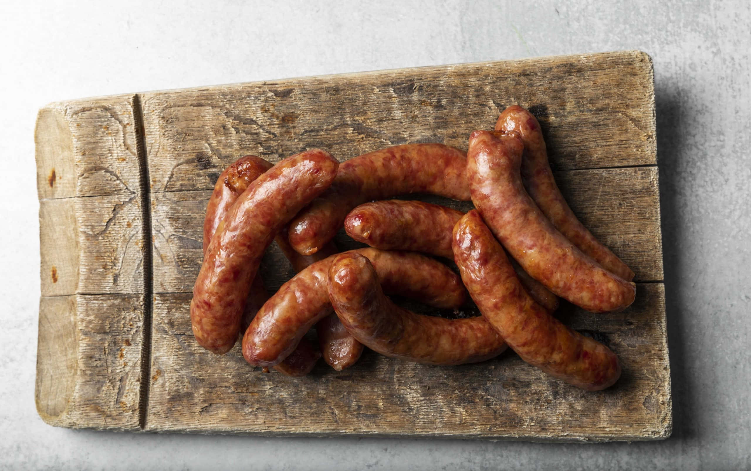 Sausage 桌布 壁紙 — 一堆光滑的棕色香腸放在一個風化的木製砧板上，背景是灰色混凝土。