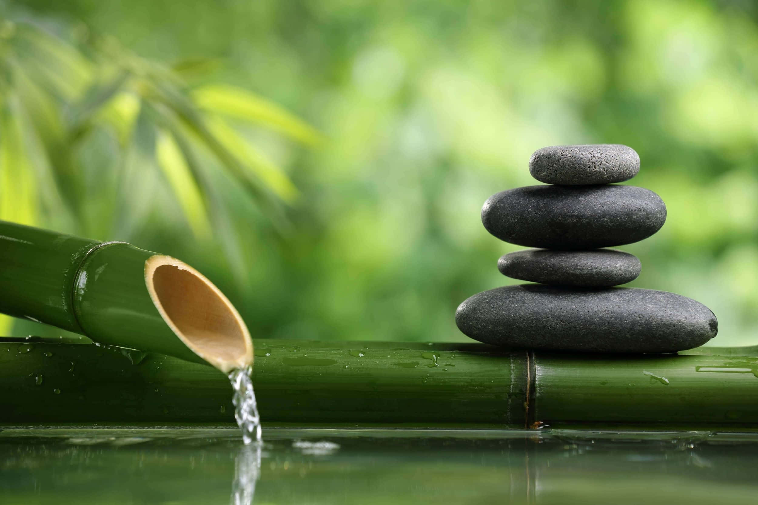 禪 桌布 壁紙 — 一堆光滑的灰色石頭平靜地平衡在竹子上，清澈的水從裂開的竹管輕輕流入反射池中。