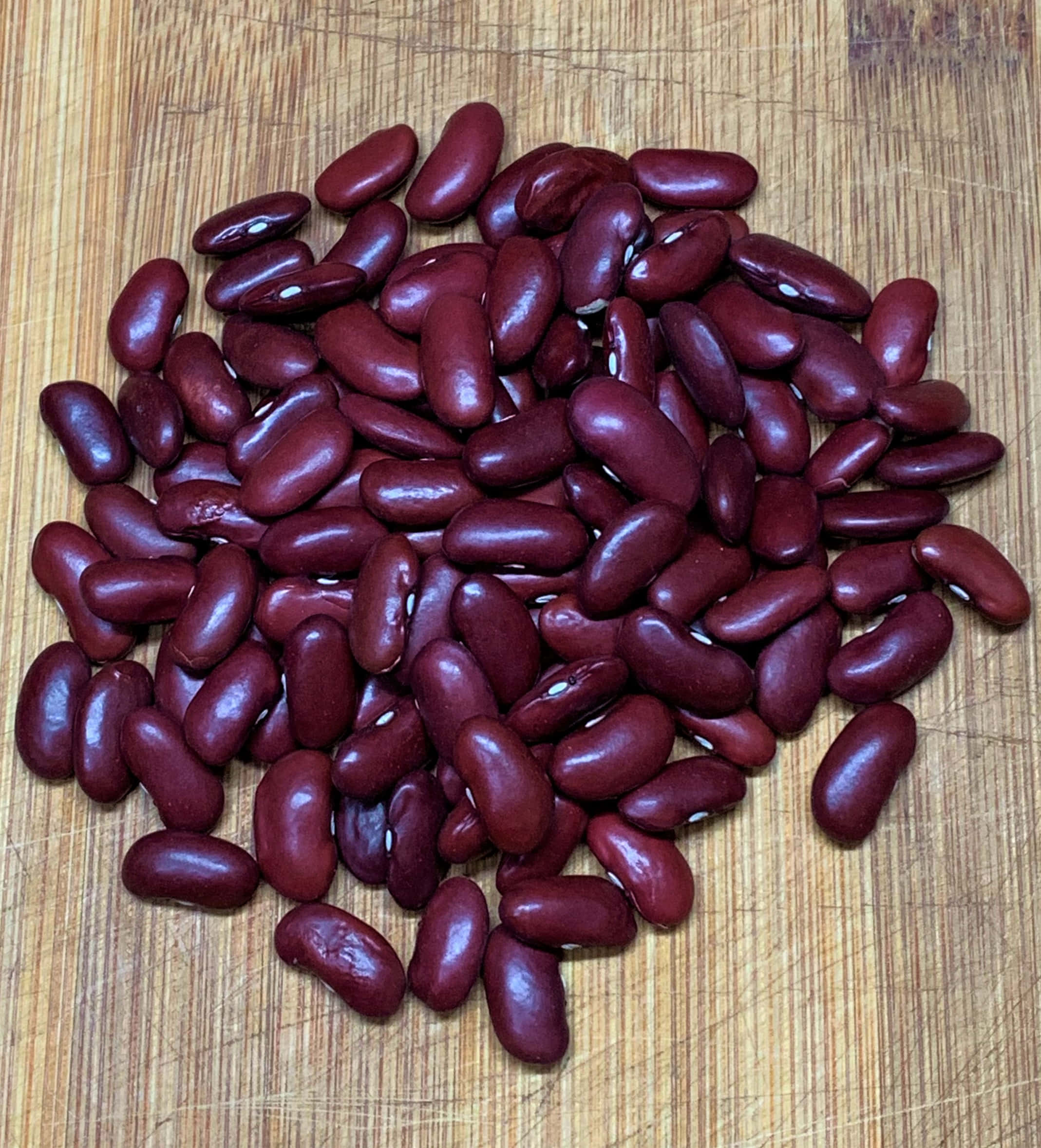 beans 桌布 壁紙 — 一堆光澤的紅腰豆放在一個磨損的木砧板上。