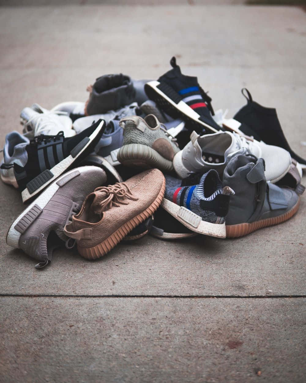 Sneakers 桌布 壁紙 — 一堆各種現代運動鞋以柔和色調放在混凝土人行道上。