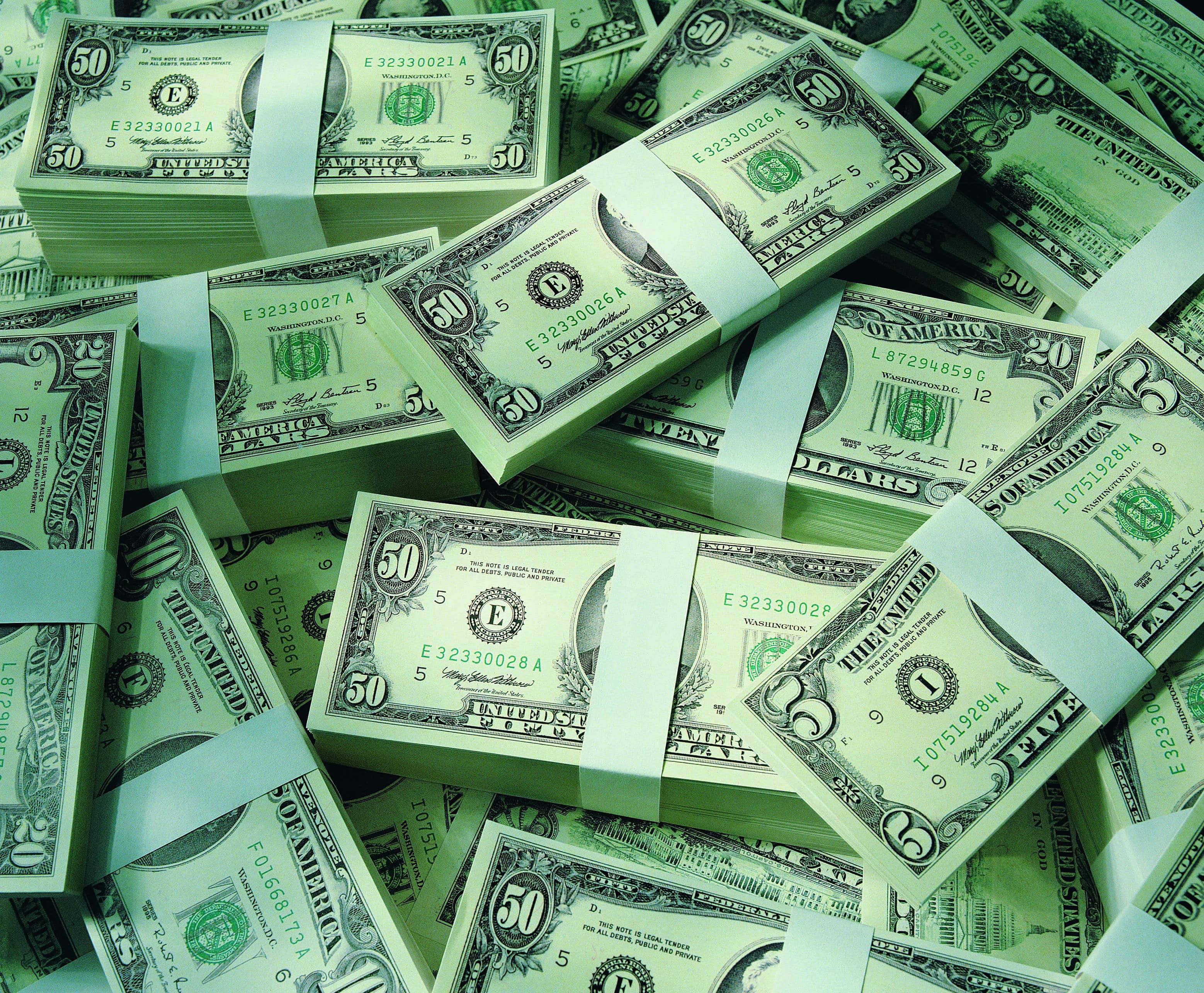 dollar 桌布 壁紙 — 一堆堆捆綁的美金鈔票，面額不同，散落在一個表面上，在冰冷的綠色燈光下。