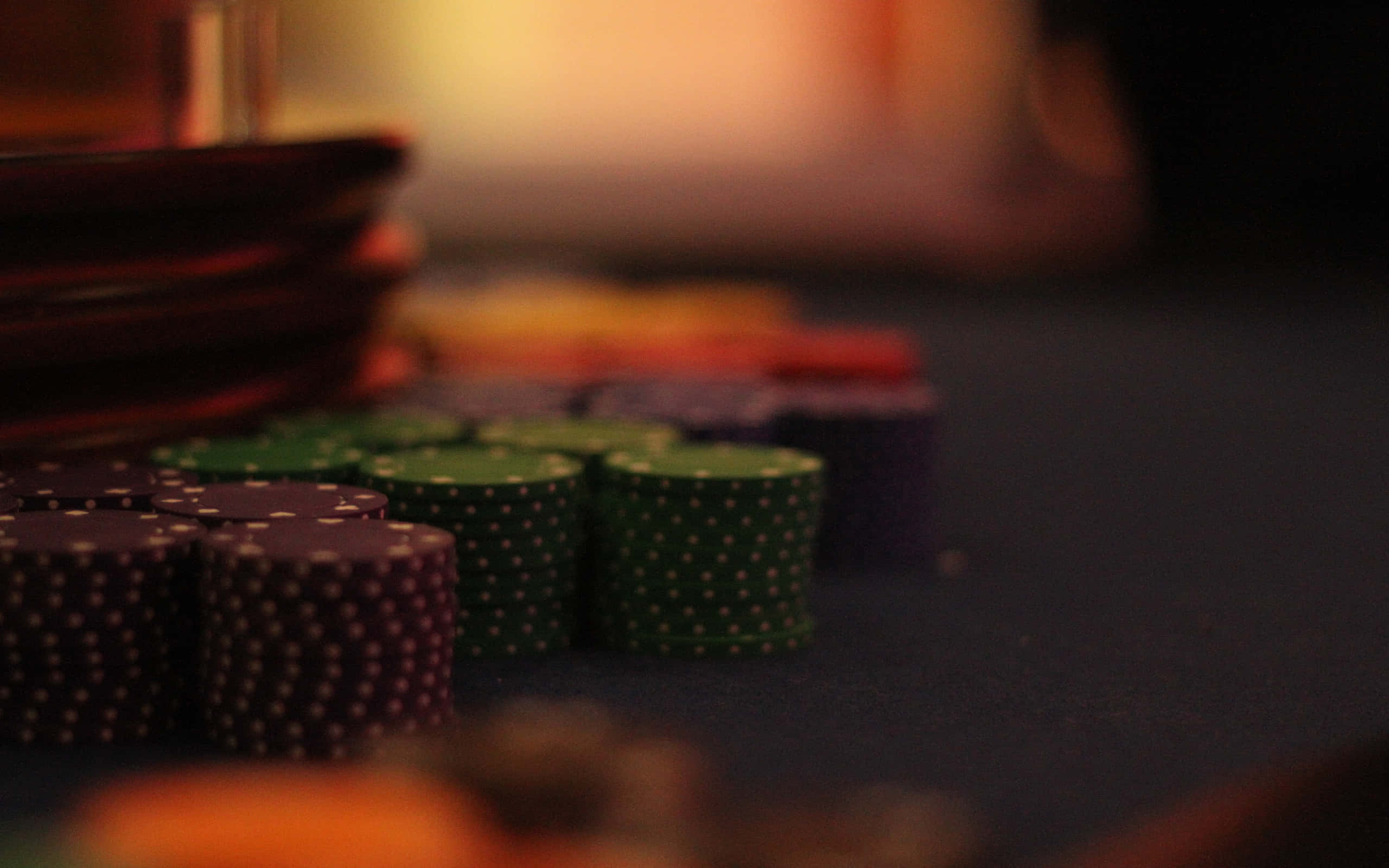 Poker 桌布 壁紙 — 一堆堆色彩繽紛的籌碼在深色氈桌上，於溫暖的環境燈光下閃耀。