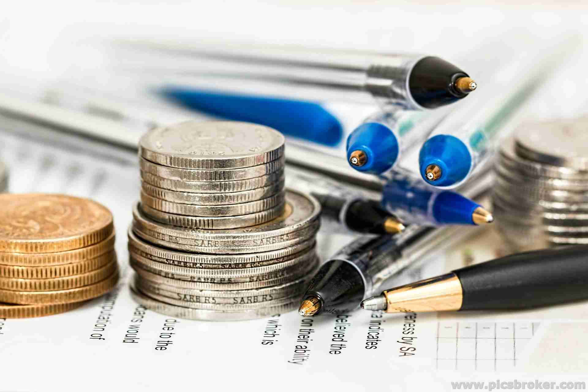金融 桌布 壁紙 — 一堆堆銀幣和金幣放在財務文件上，周圍有各種筆，景深較淺。