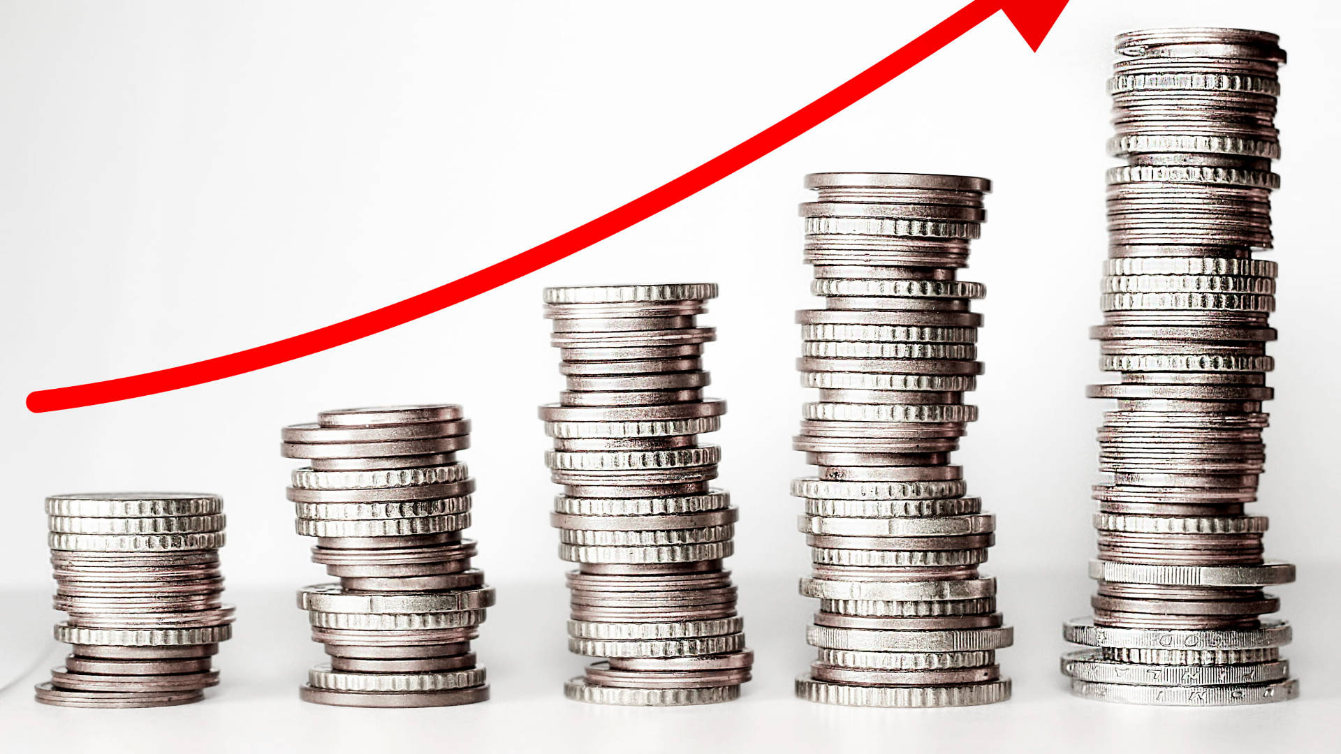 Money 桌布 壁紙 — 一堆堆銀幣逐漸升高，並有一個粗體的紅色向上箭頭，象徵財務增長。