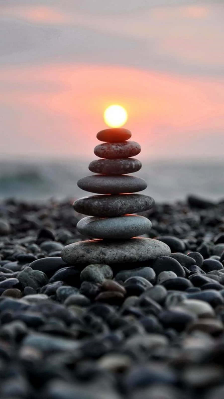 禪 桌布 壁紙 — 一堆完美平滑的石頭在鵝卵石海灘上保持平衡，夕陽在後方落下，投射出溫暖的光芒。