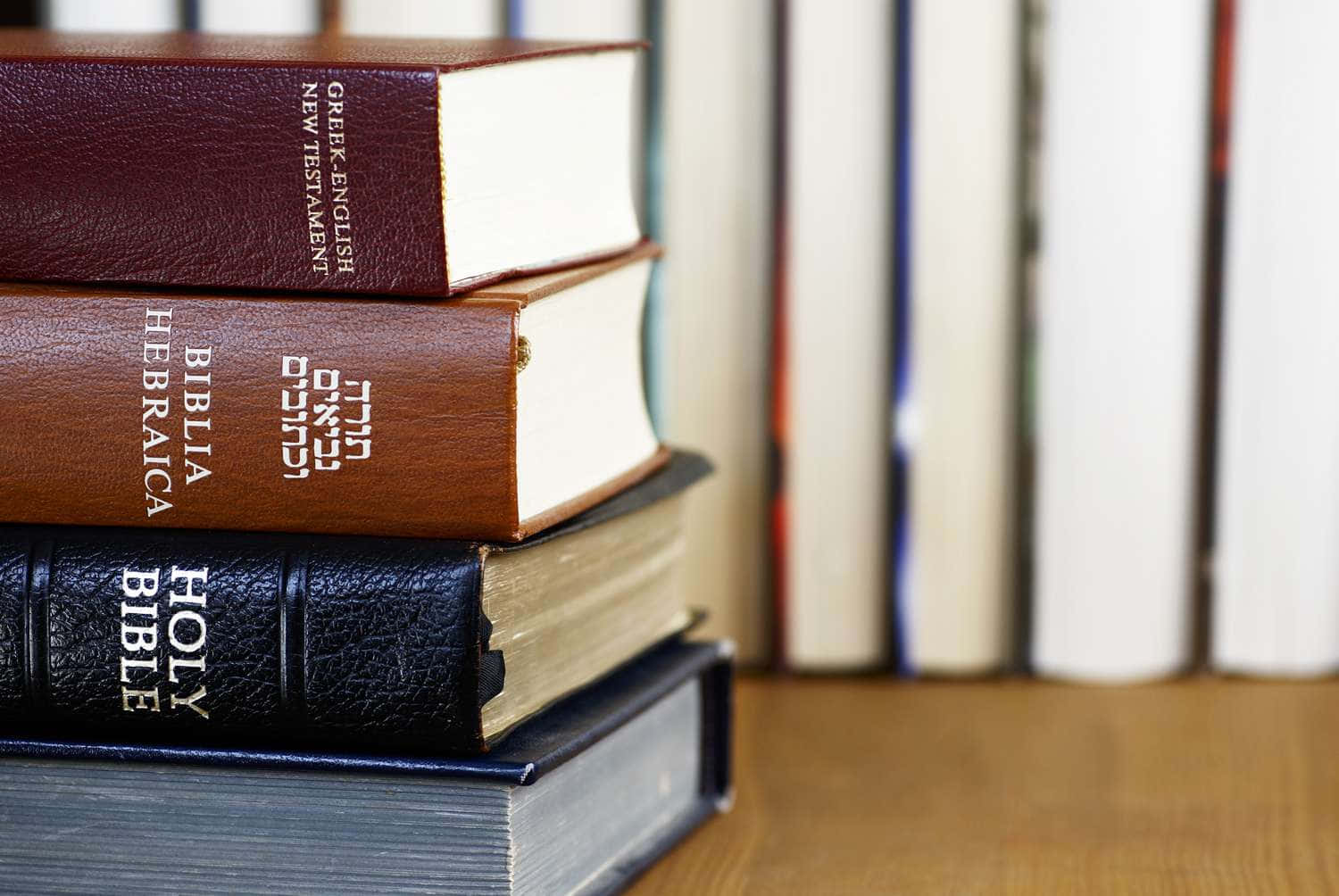 聖經 桌布 壁紙 — 一堆宗教書籍，包括希臘文-英文新約聖經和希伯來文聖經，放在木質表面上。
