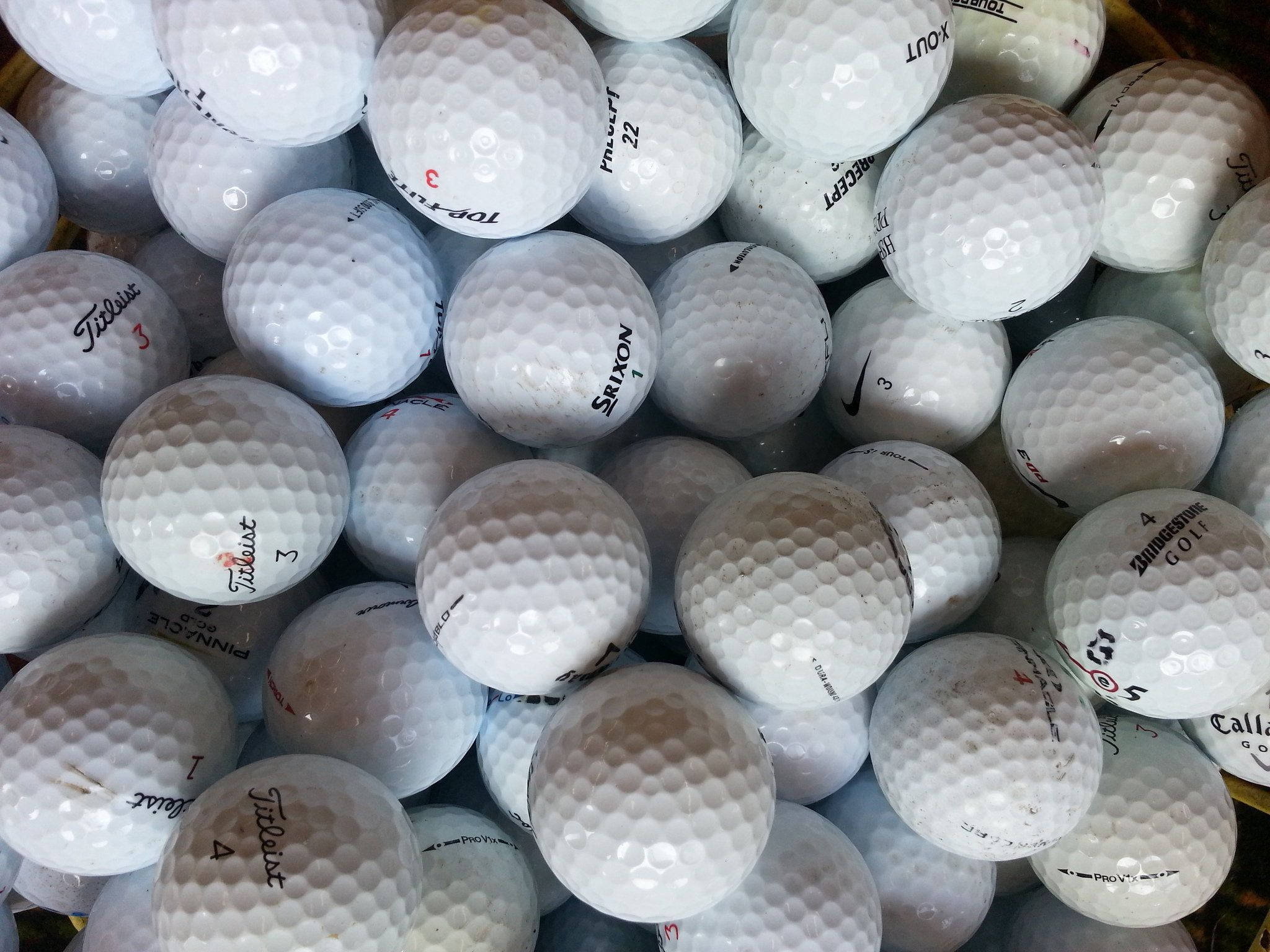 Golfing 桌布 壁紙 — 一堆密集的白色高爾夫球，帶有明顯的品牌標記和刮痕，在明亮燈光下。