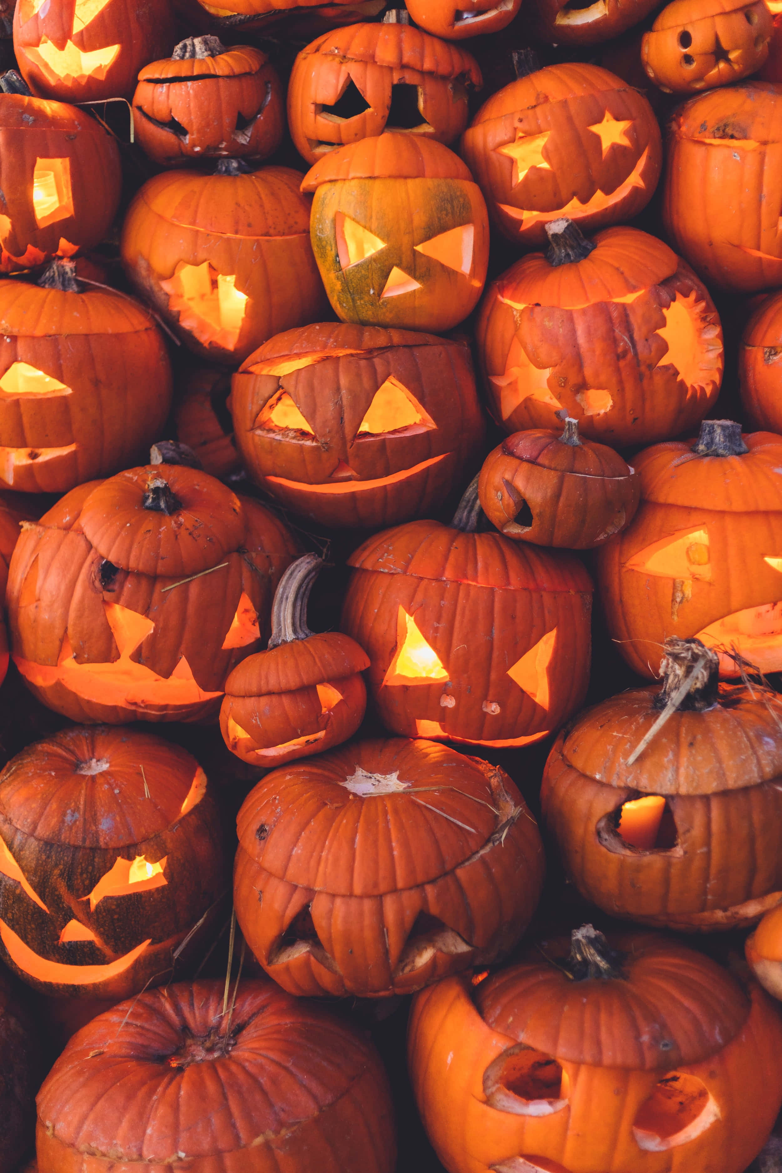 jack o'lantern 桌布 壁紙 — 一堆密集的雕刻萬聖節南瓜，內部閃爍的燭光溫暖地發光。