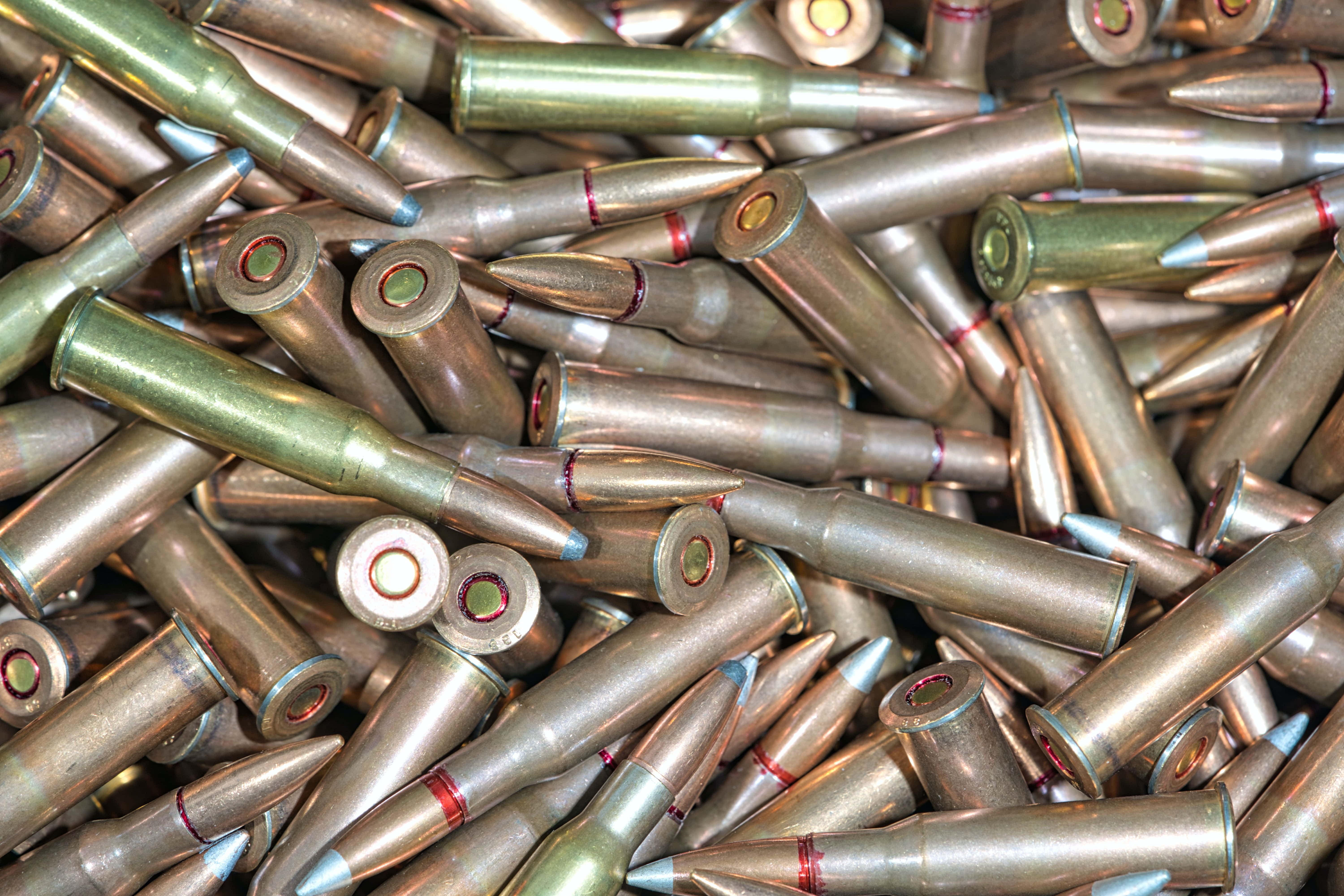 bullet 桌布 壁紙 — 一堆密集的黃銅步槍子彈，帶有紅色和藍色標記，混亂地散落在特寫鏡頭中。