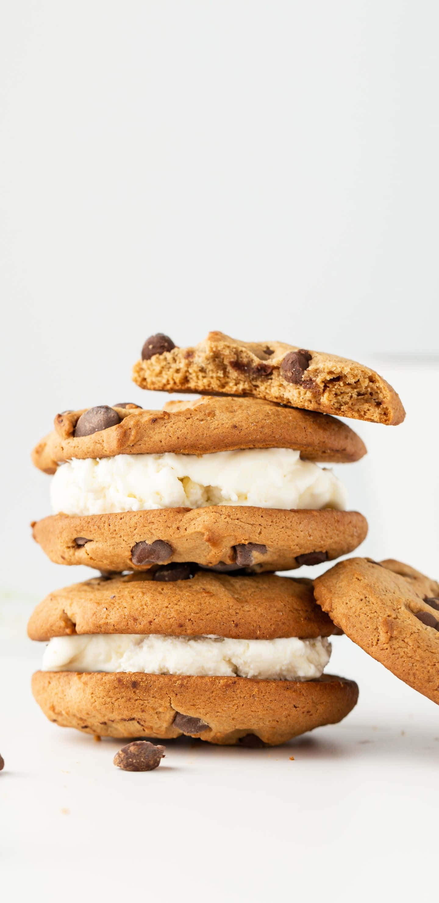Chocolate Chip Cookie 桌布 壁紙 — 一堆巧克力餅乾三明治，夾著香滑香草冰淇淋，放在明亮的白色背景上。