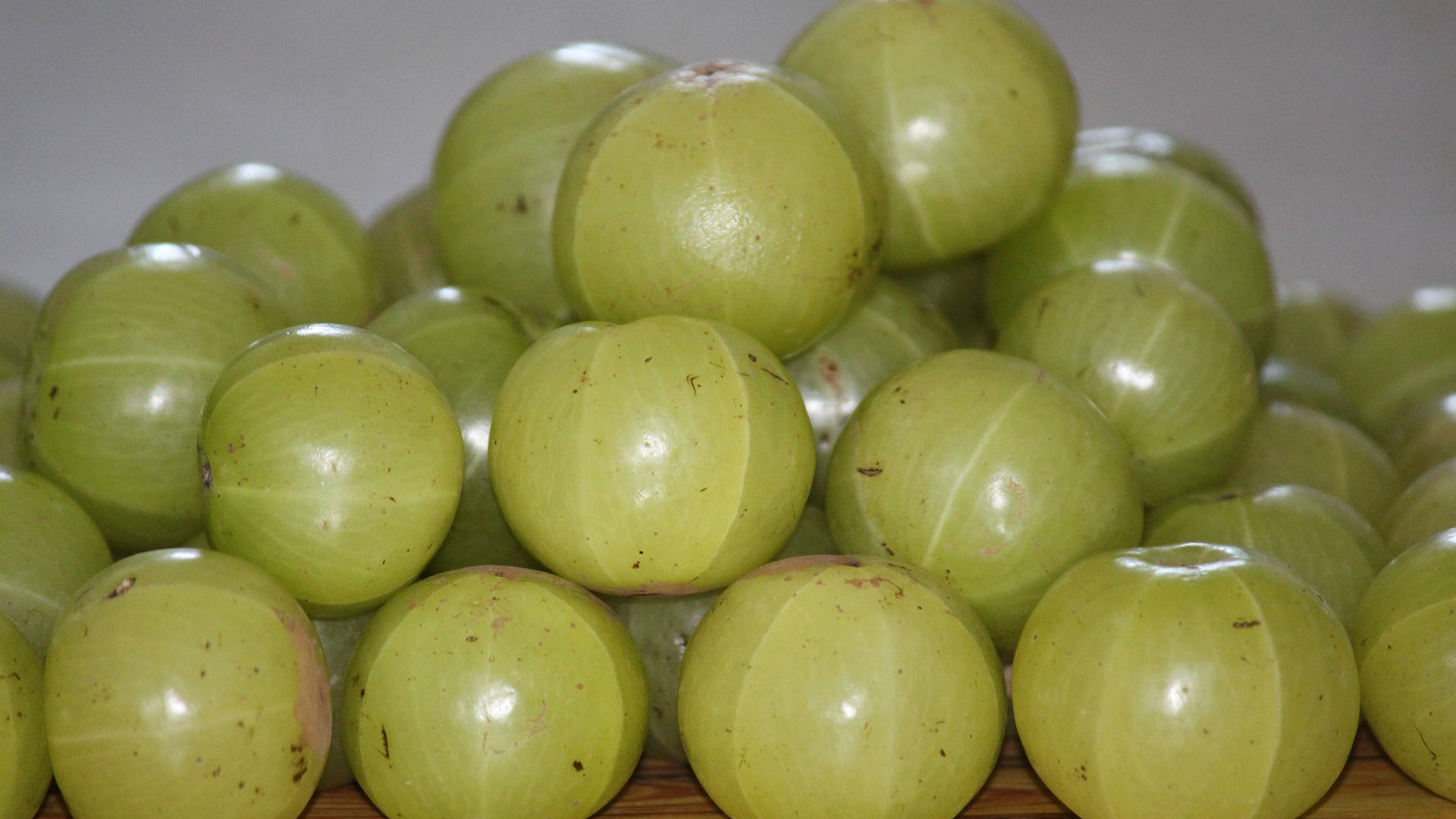 Fruits 桌布 壁紙 — 一堆帶有細微條紋和小瑕疵的光澤綠色鵝莓特寫，放在木質表面上。