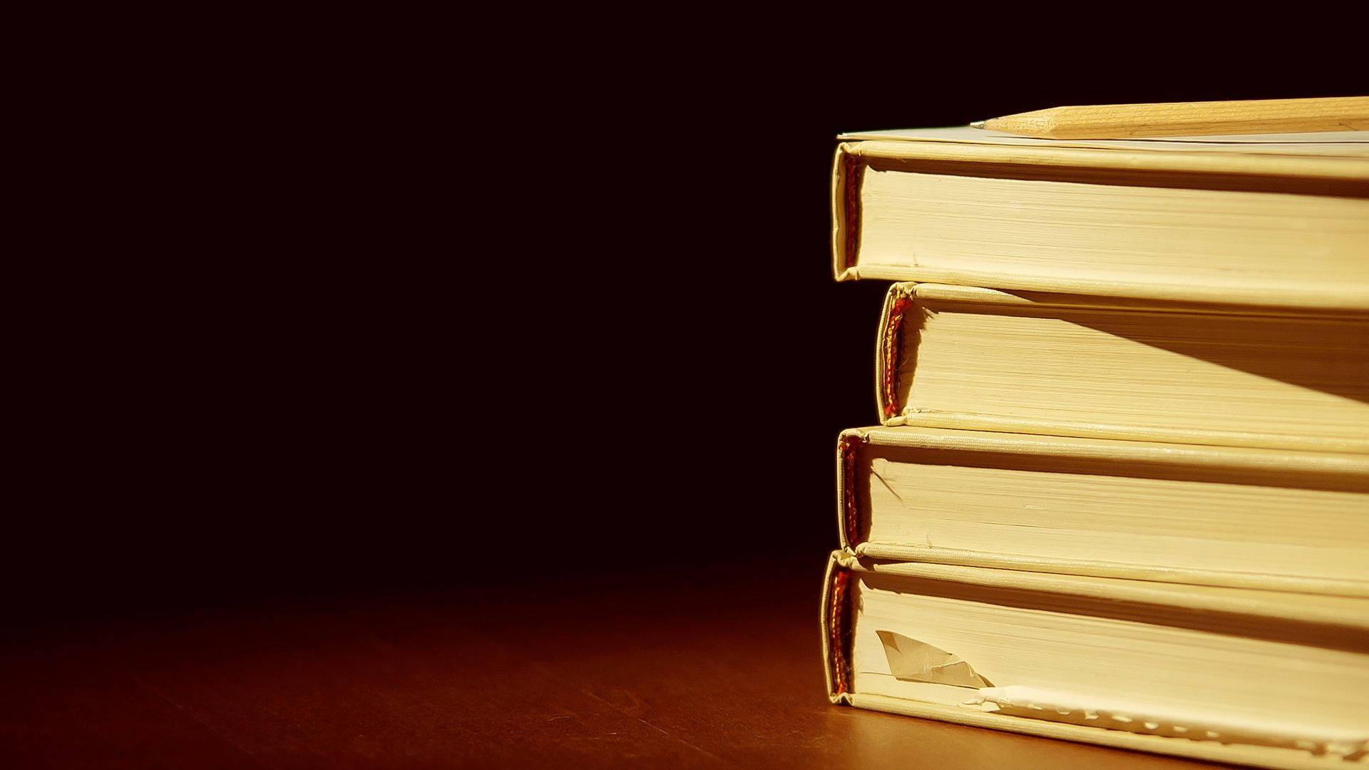 書本 桌布 壁紙 — 一堆復古書籍沐浴在溫暖的金色光線中，背景為深色。