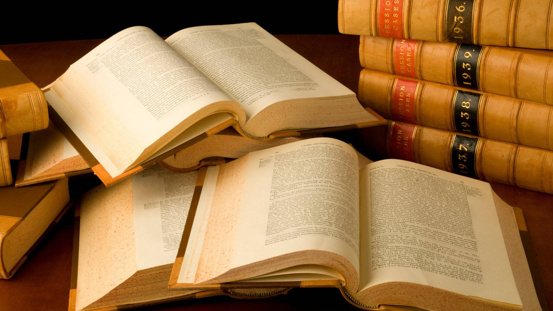 復古 桌布 壁紙 — 一堆復古皮革裝訂的法律書籍，打開的書頁在木桌上柔和燈光下溫暖地發光。