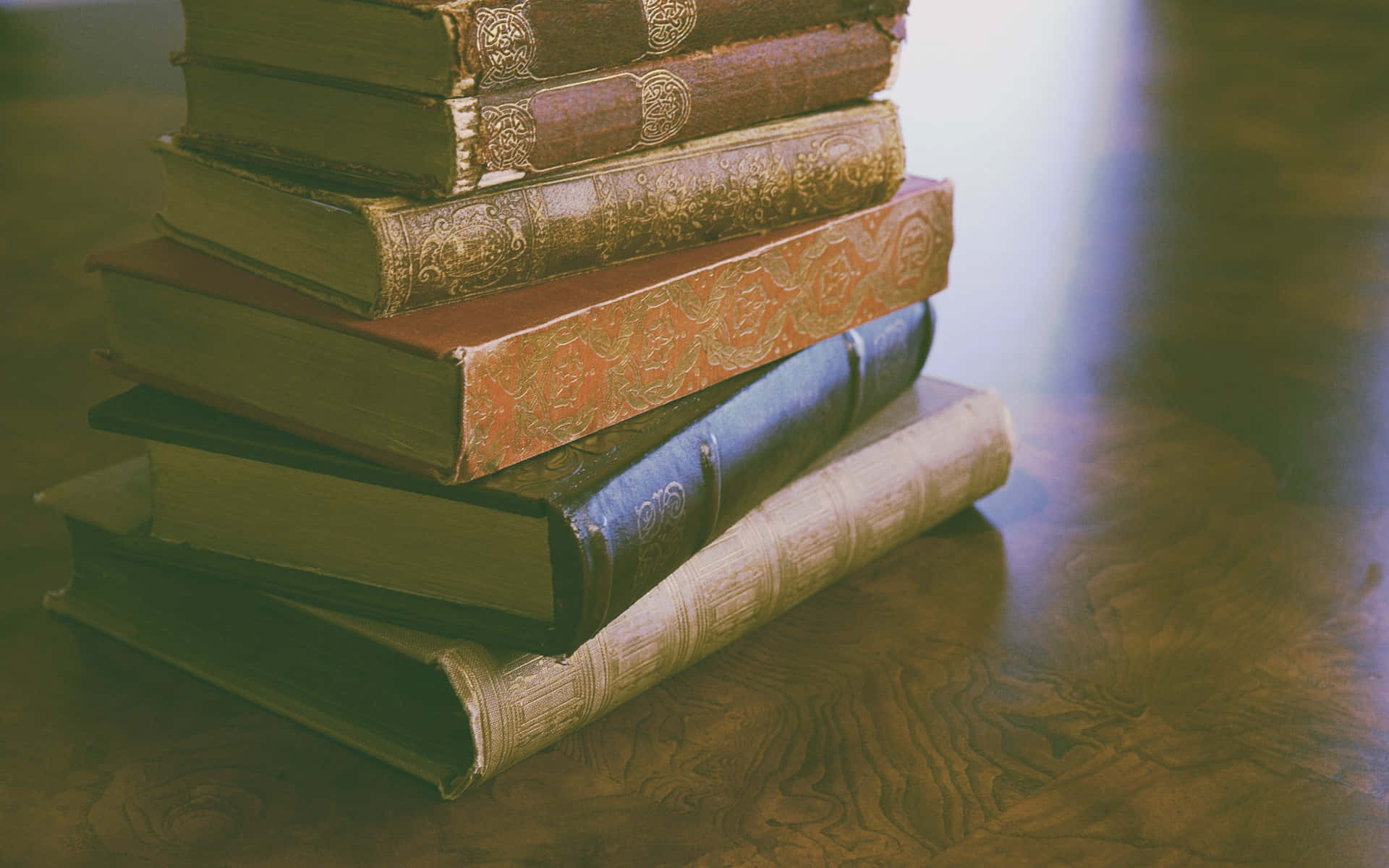 書本 桌布 壁紙 — 一堆復古裝飾書籍放在拋光木桌上，沐浴在溫暖的金色光線中。