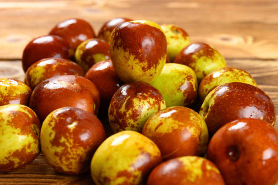 Fruits 桌布 壁紙 — 一堆成熟的紅棗，帶有斑駁的紅色和黃色果皮，放在溫暖的木質表面上。