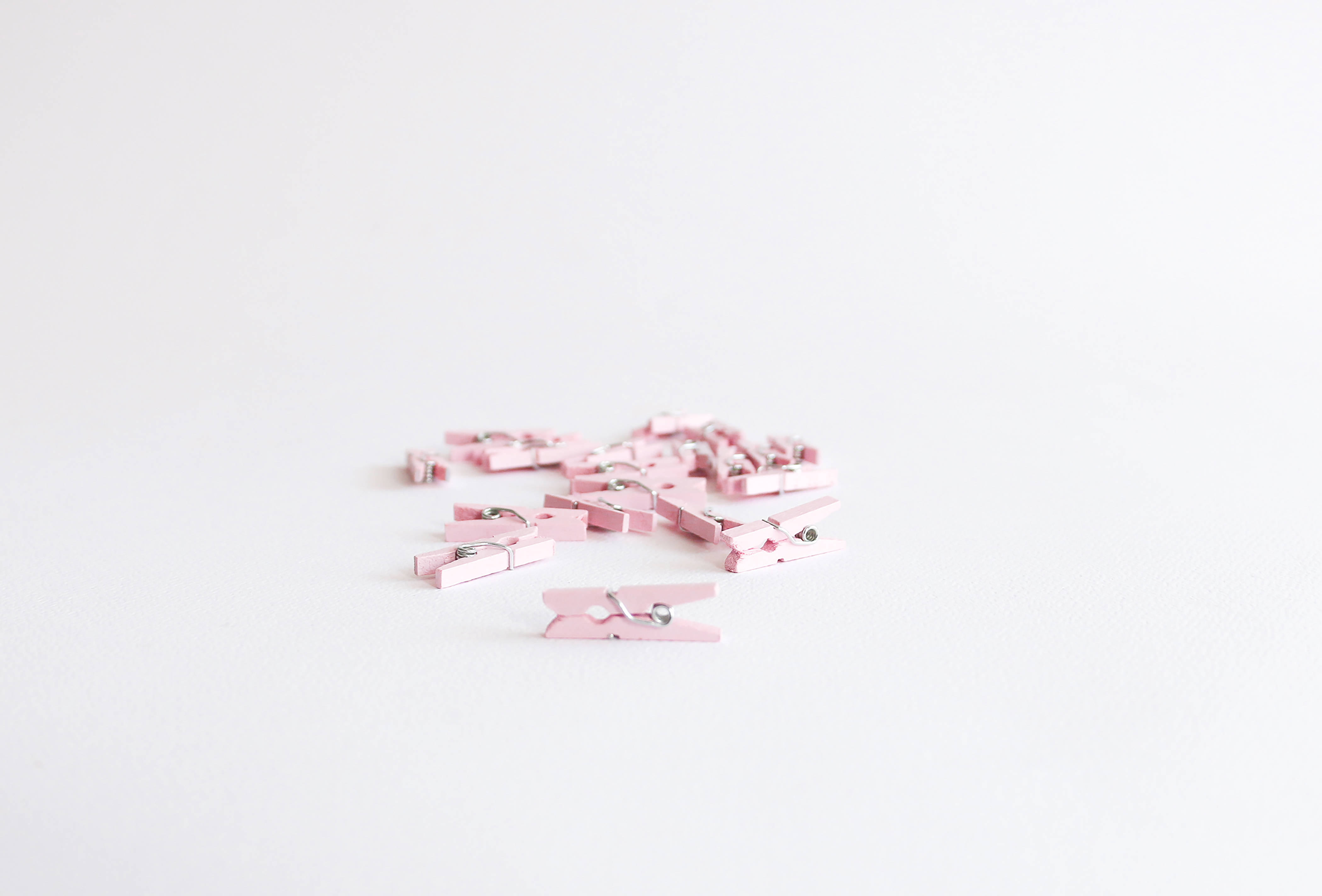 girly pink aesthetic 桌布 壁紙 — 一堆散落的小粉紅色木衣夾放在純白色表面上。