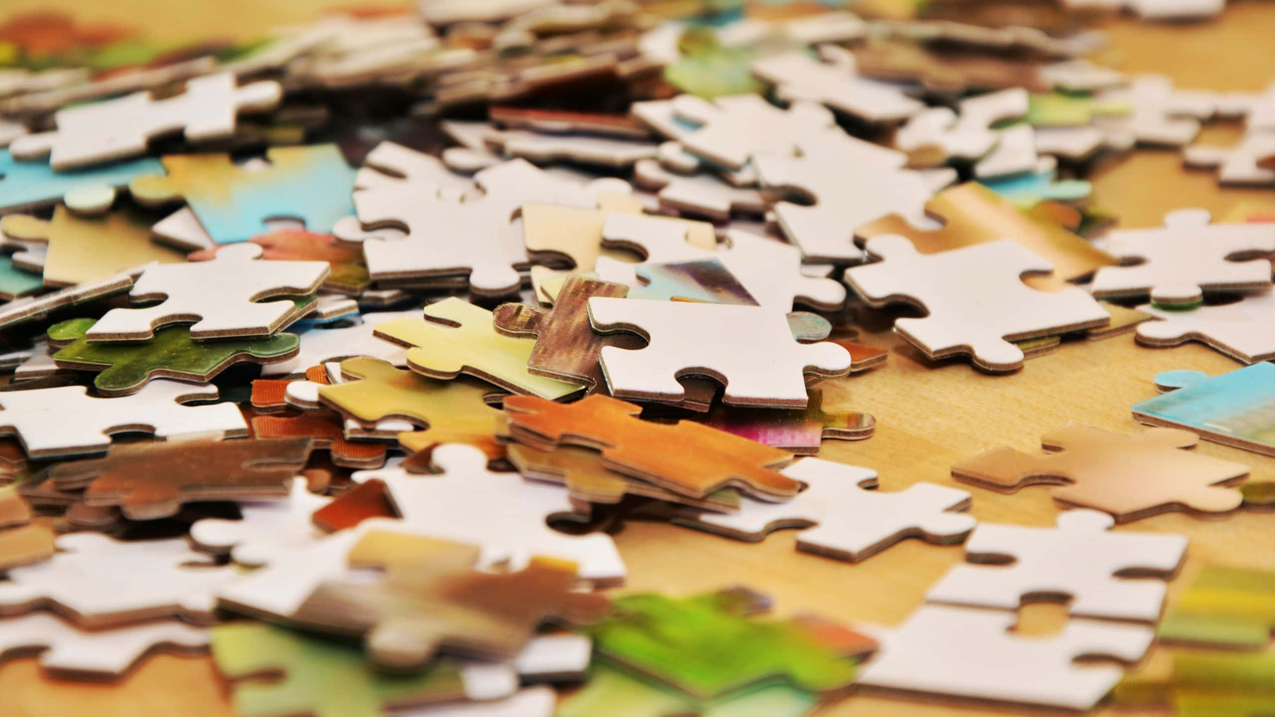 Puzzle Games 桌布 壁紙 — 一堆散落的彩色拼圖碎片放在溫暖的木質表面上，景深較淺。
