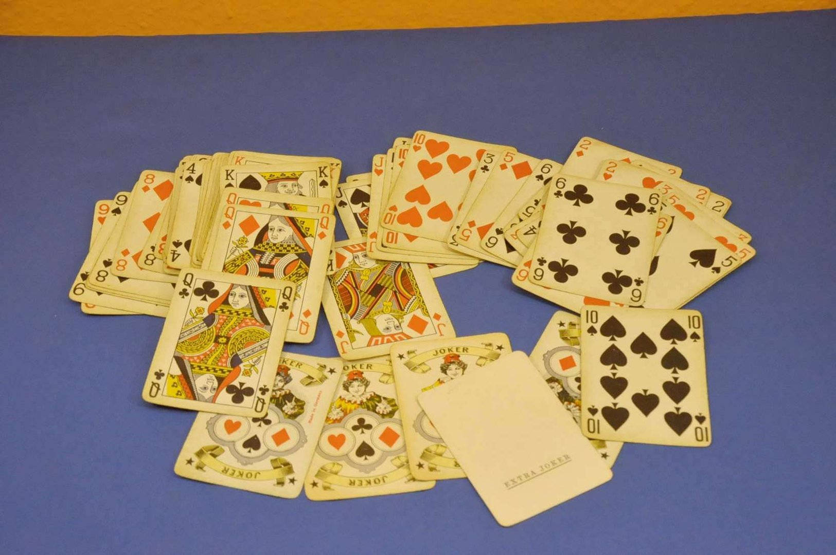 Playing Cards 桌布 壁紙 — 一堆散落的復古撲克牌，包含小丑牌和人頭牌，在溫暖燈光下置於藍色表面上。