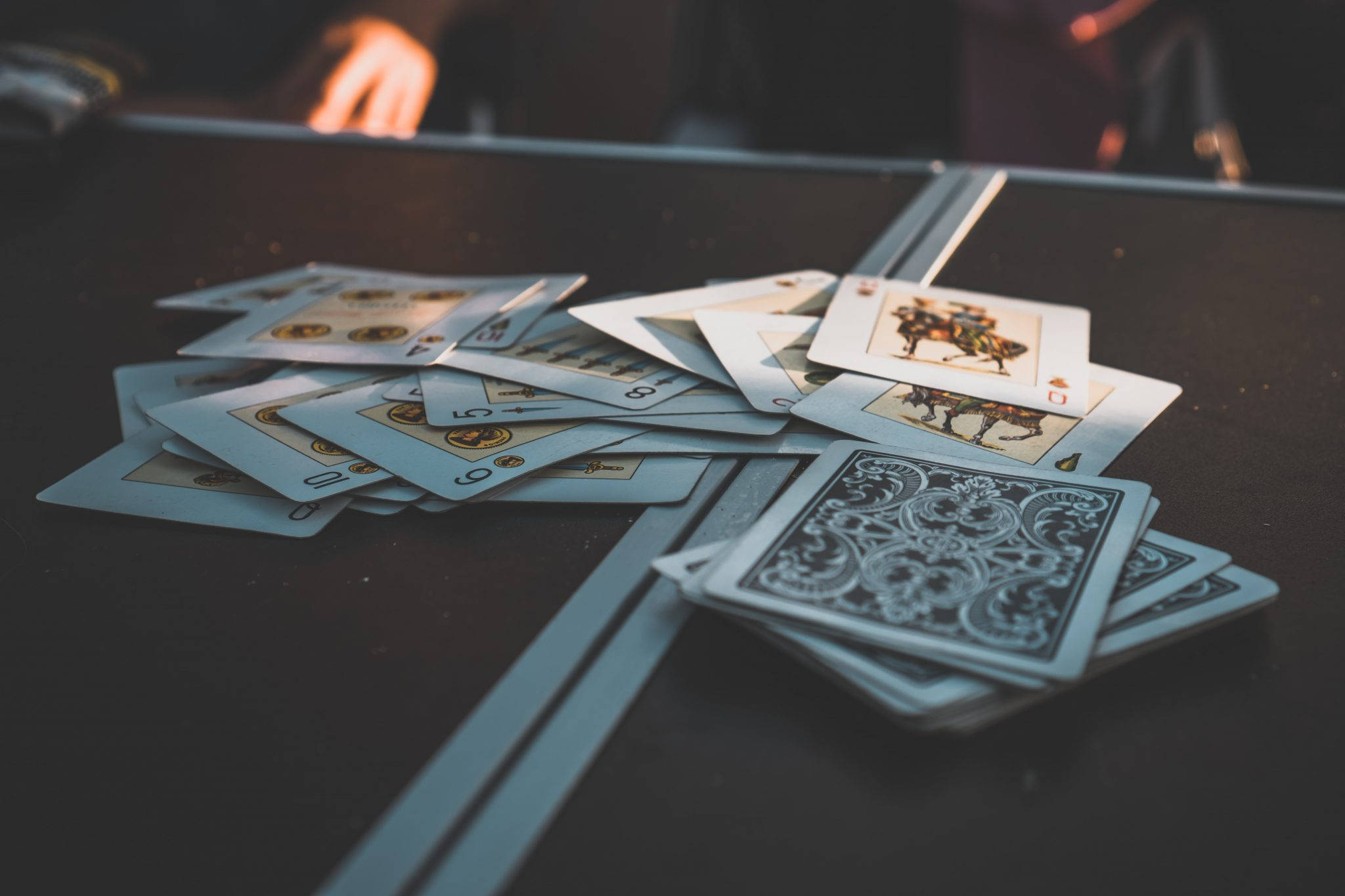 Playing Cards 桌布 壁紙 — 一堆散落的撲克牌放在深色桌子上，背景有一隻模糊的手。