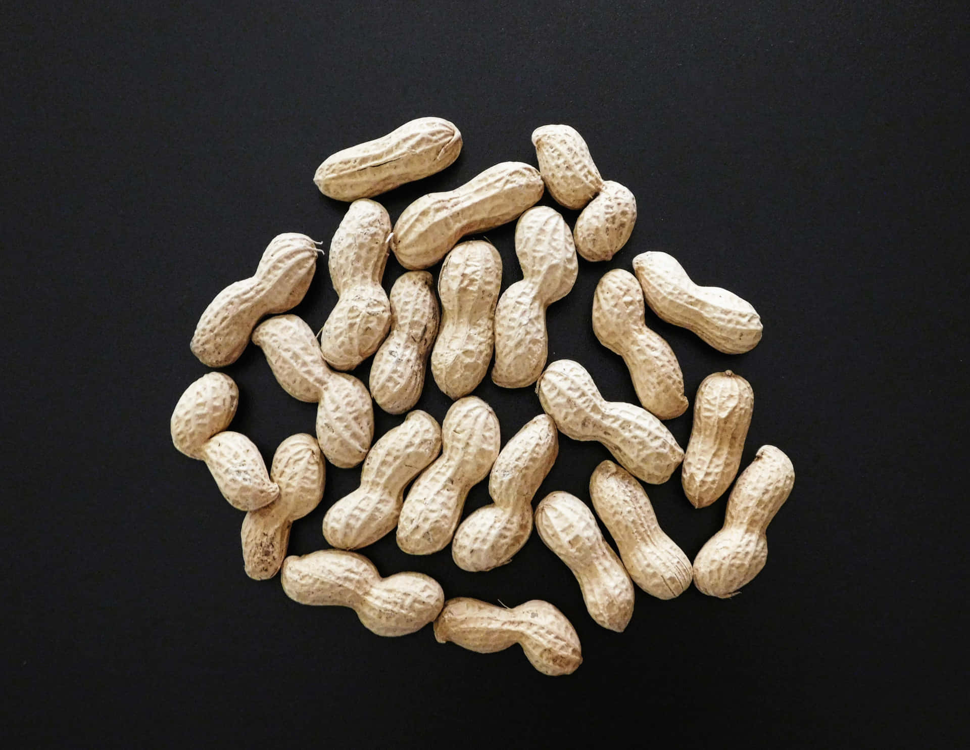 Peanuts 壁紙 — 一堆散落的生花生連殼放在光滑的黑色表面上。