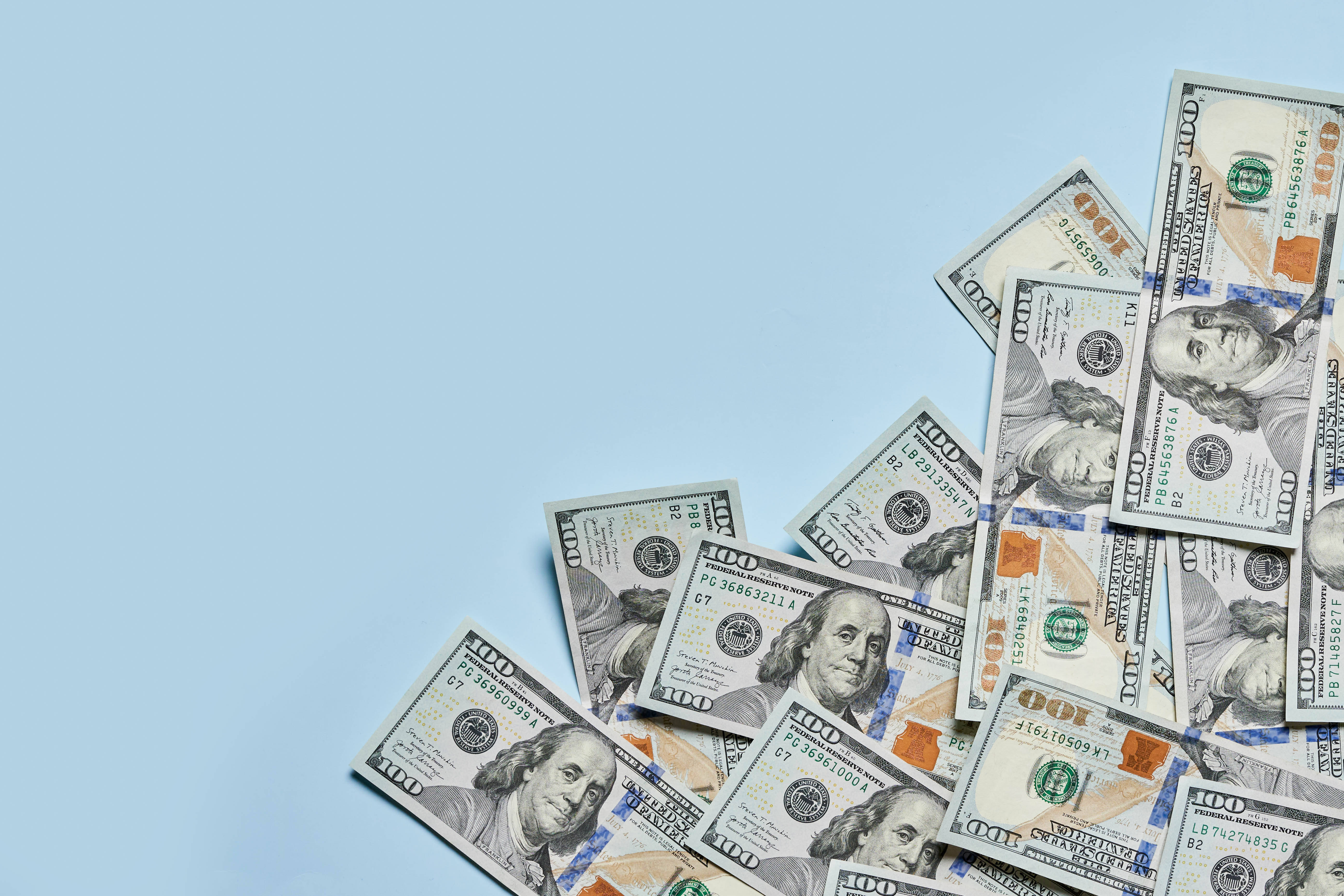 No Money 桌布 壁紙 — 一堆散落的百元美鈔灑在純淺藍色背景上，留有大量空白空間。