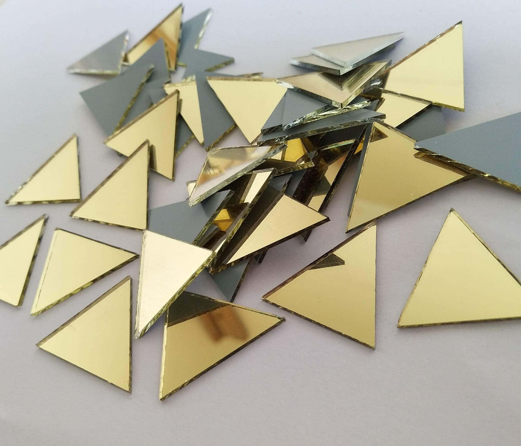 Yellow Triangle 桌布 壁紙 — 一堆散落的金色和銀色三角形鏡子碎片，在純白色表面上反射光線。