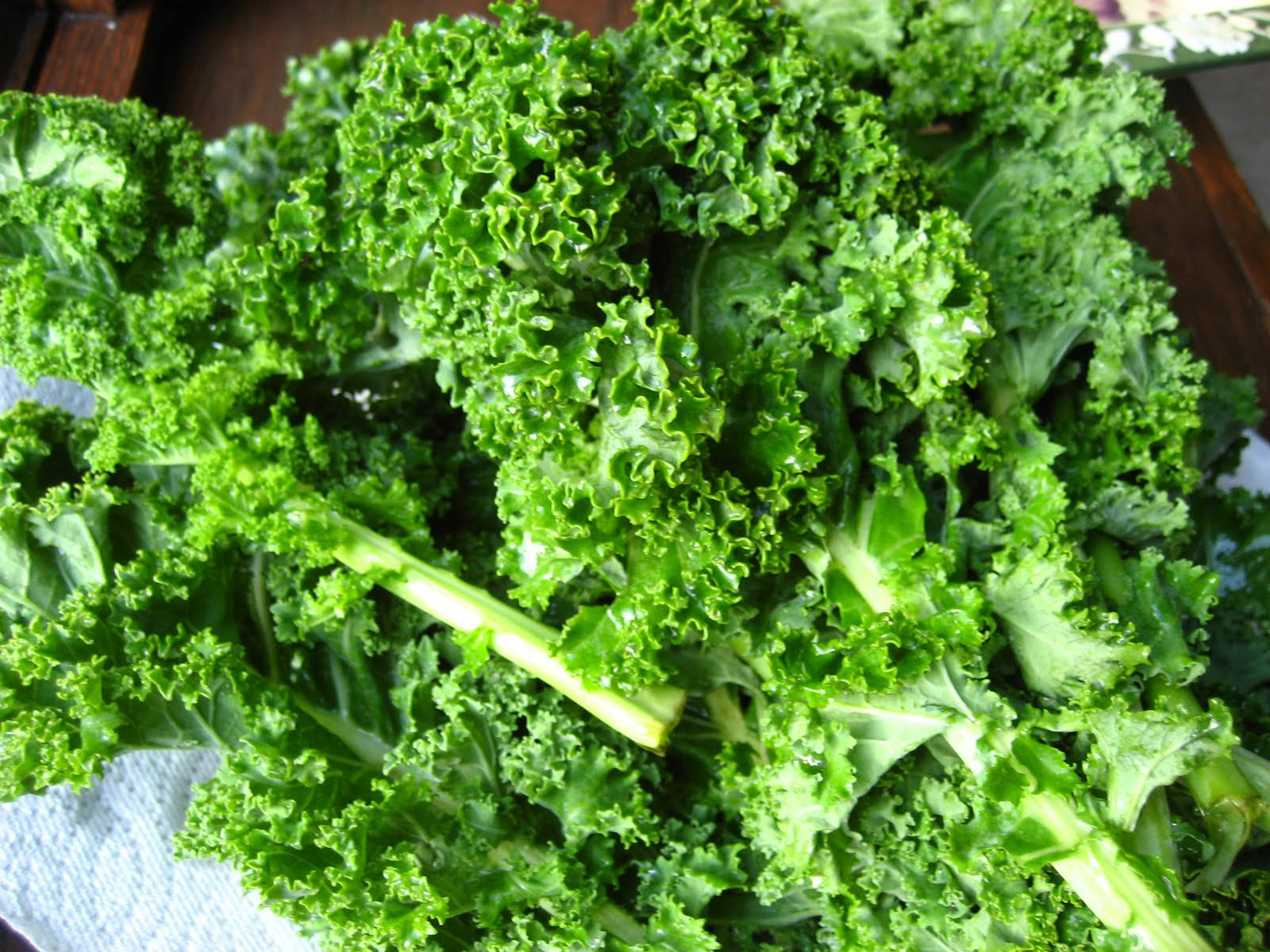 Cabbage 桌布 壁紙 — 一堆新鮮的羽衣甘藍葉，邊緣捲曲，莖部翠綠，放在木質表面上，充滿活力。