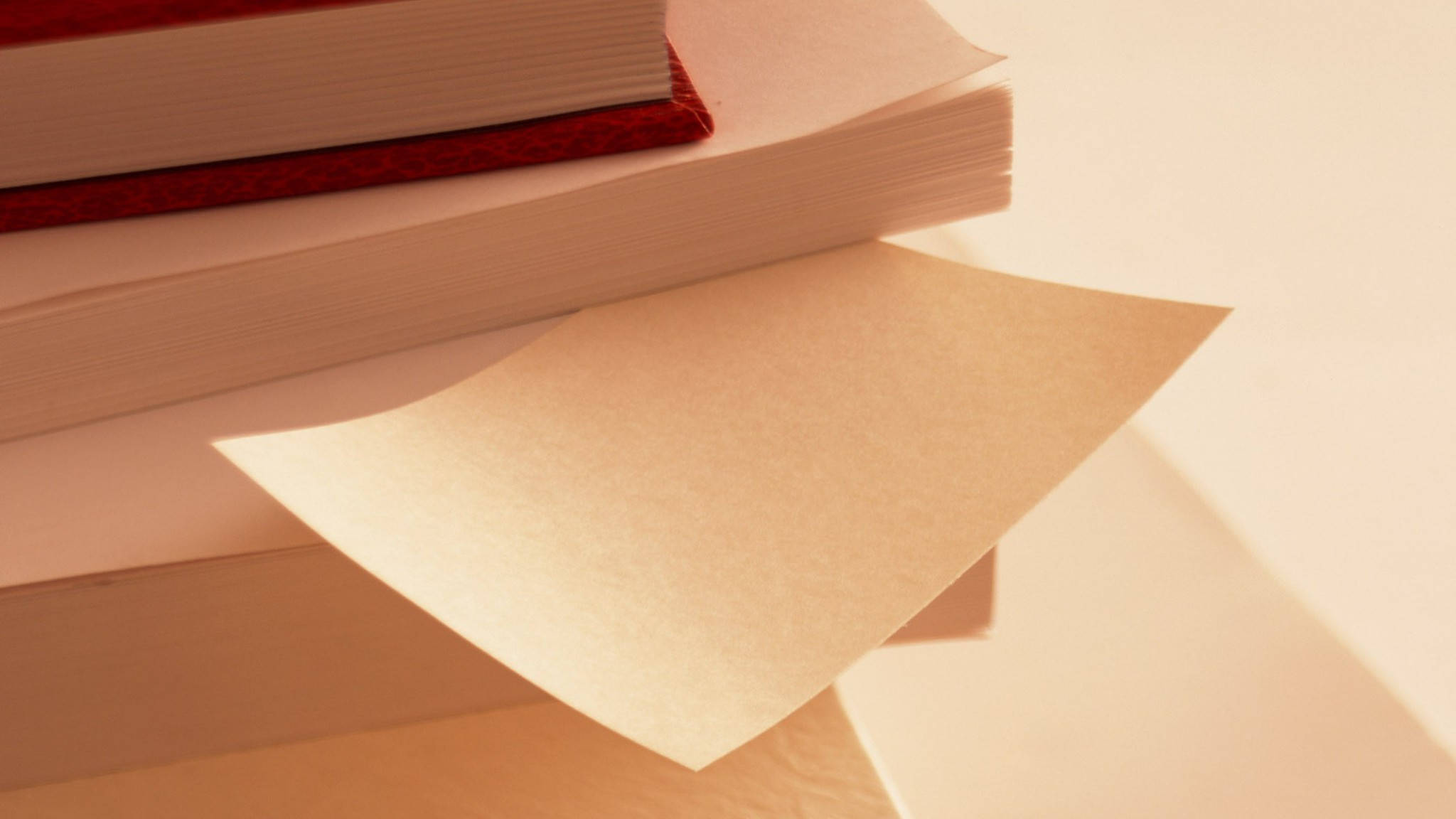 教育 桌布 壁紙 — 一堆書，單張紙在溫暖的金色燈光下呈扇形展開。